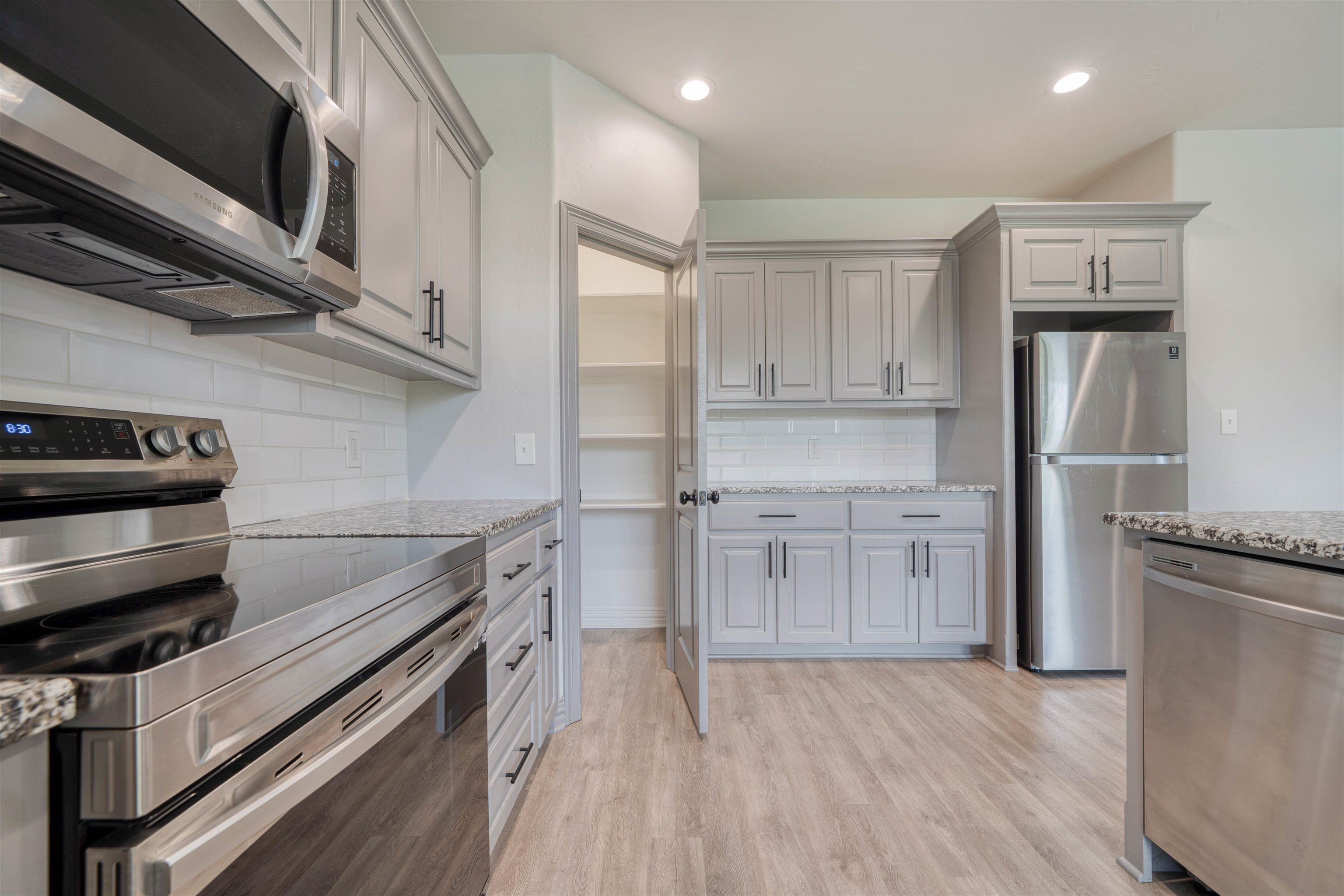 Kitchen with gray cabinets, subway-tile backsplash, granite counters, stainless appliances, and an open pantry.