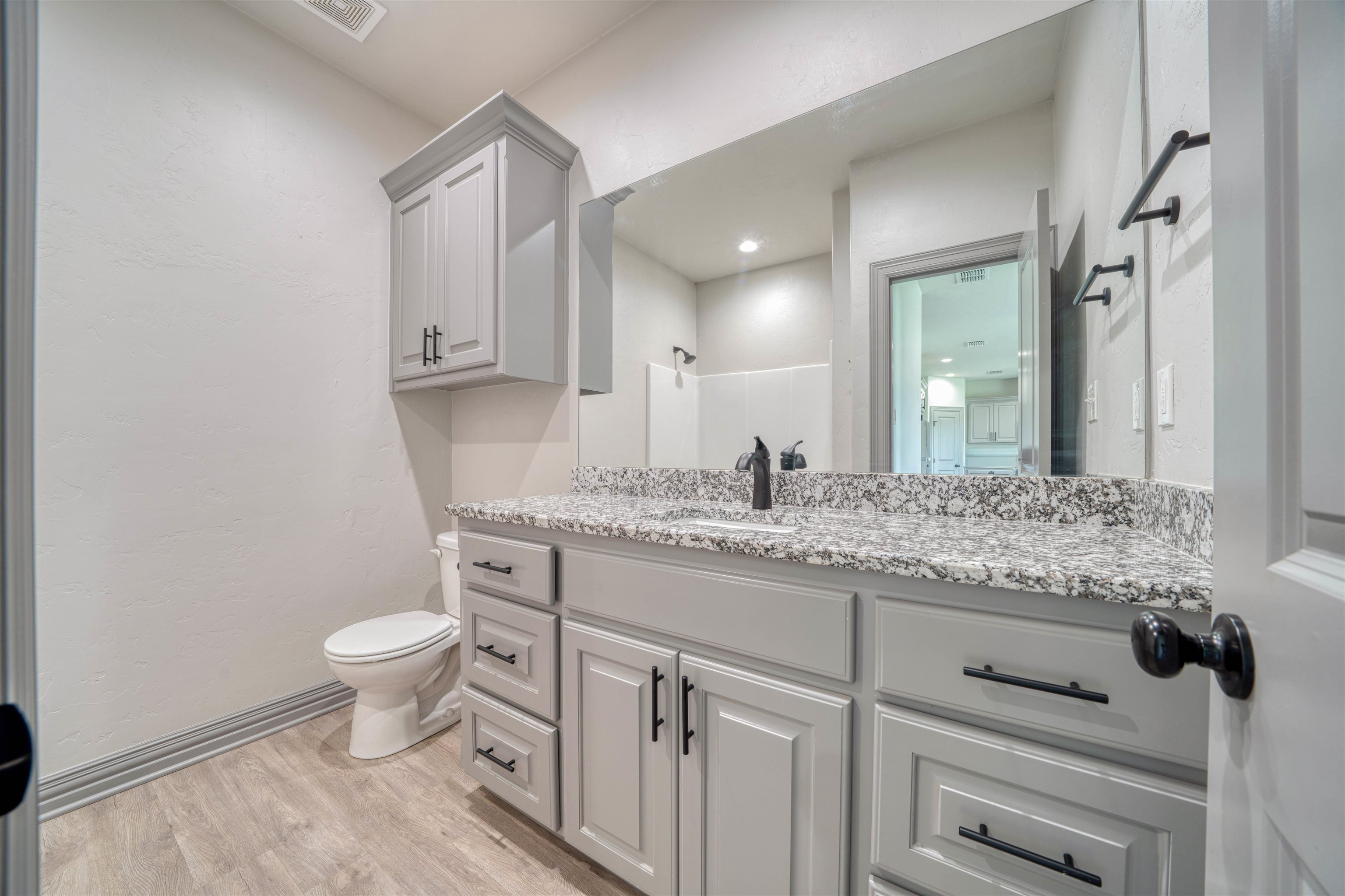 Bathroom with a gray vanity, speckled granite countertop, large mirror, and toilet.