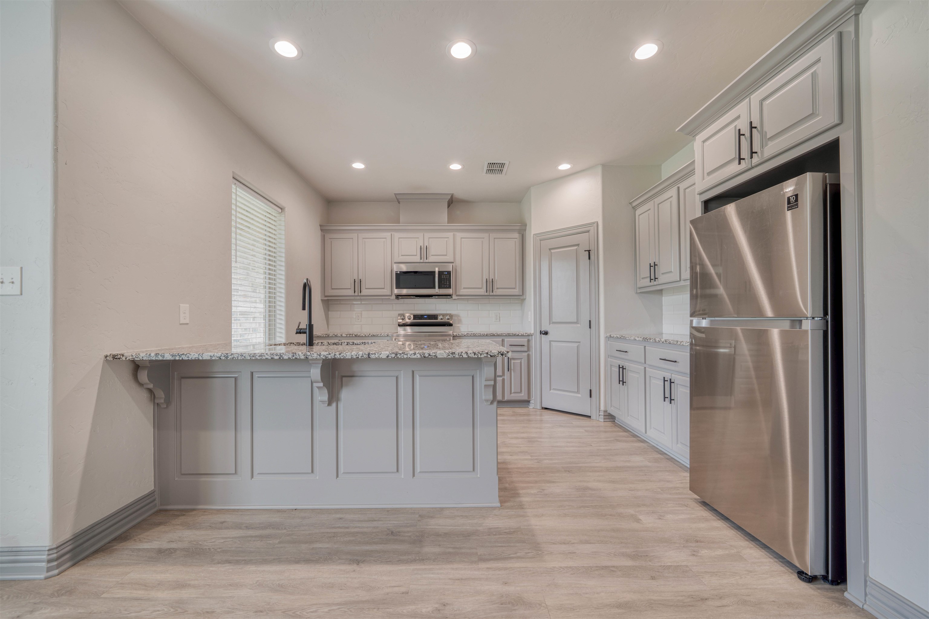 Kitchen with white cabinets, granite island, stainless steel appliances, and light wood-look flooring.