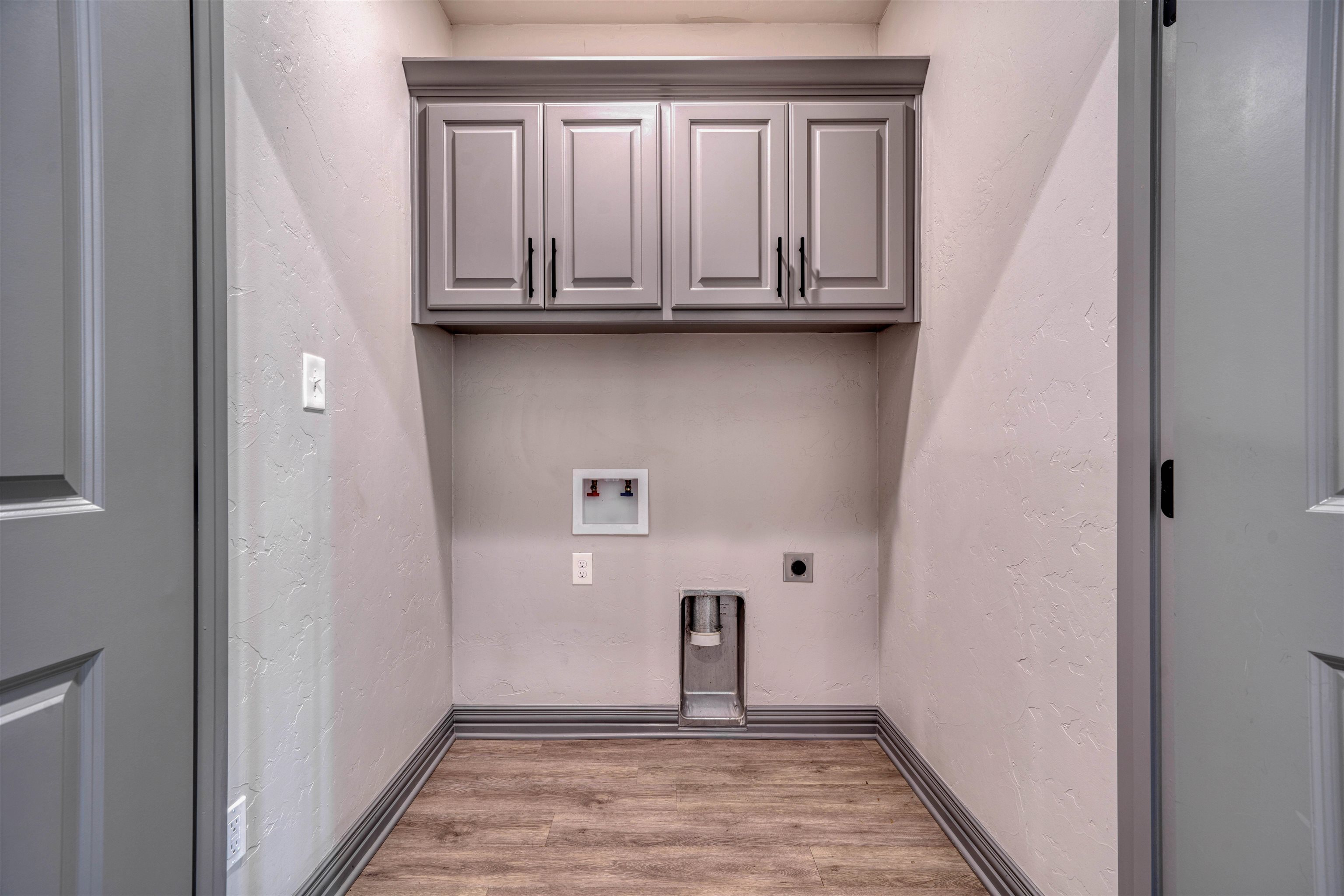 Laundry alcove with gray cabinets, washer and dryer hookups, and wood-look flooring.