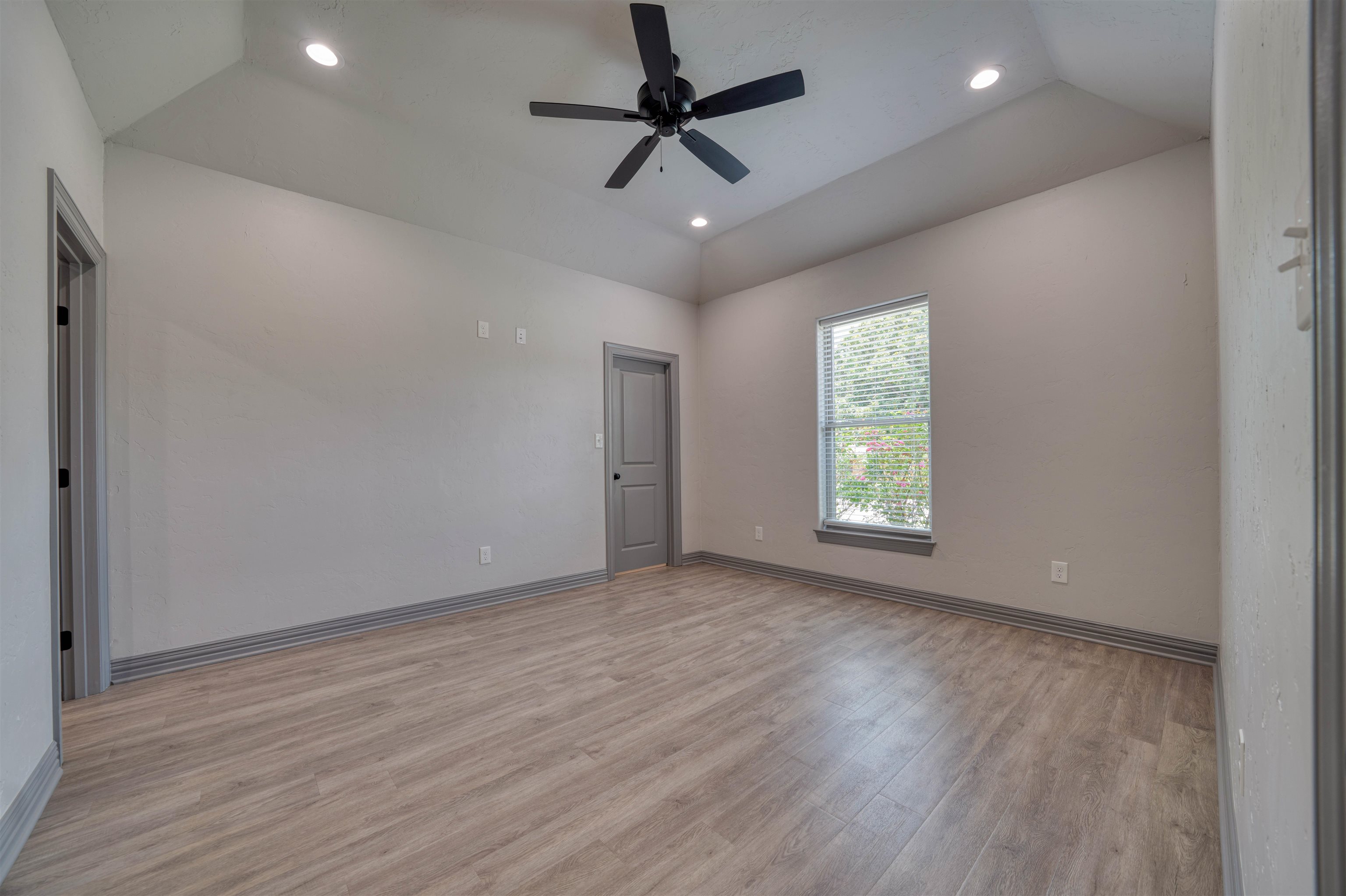 Empty bedroom with wood-look floors, a black ceiling fan, and a window with blinds.