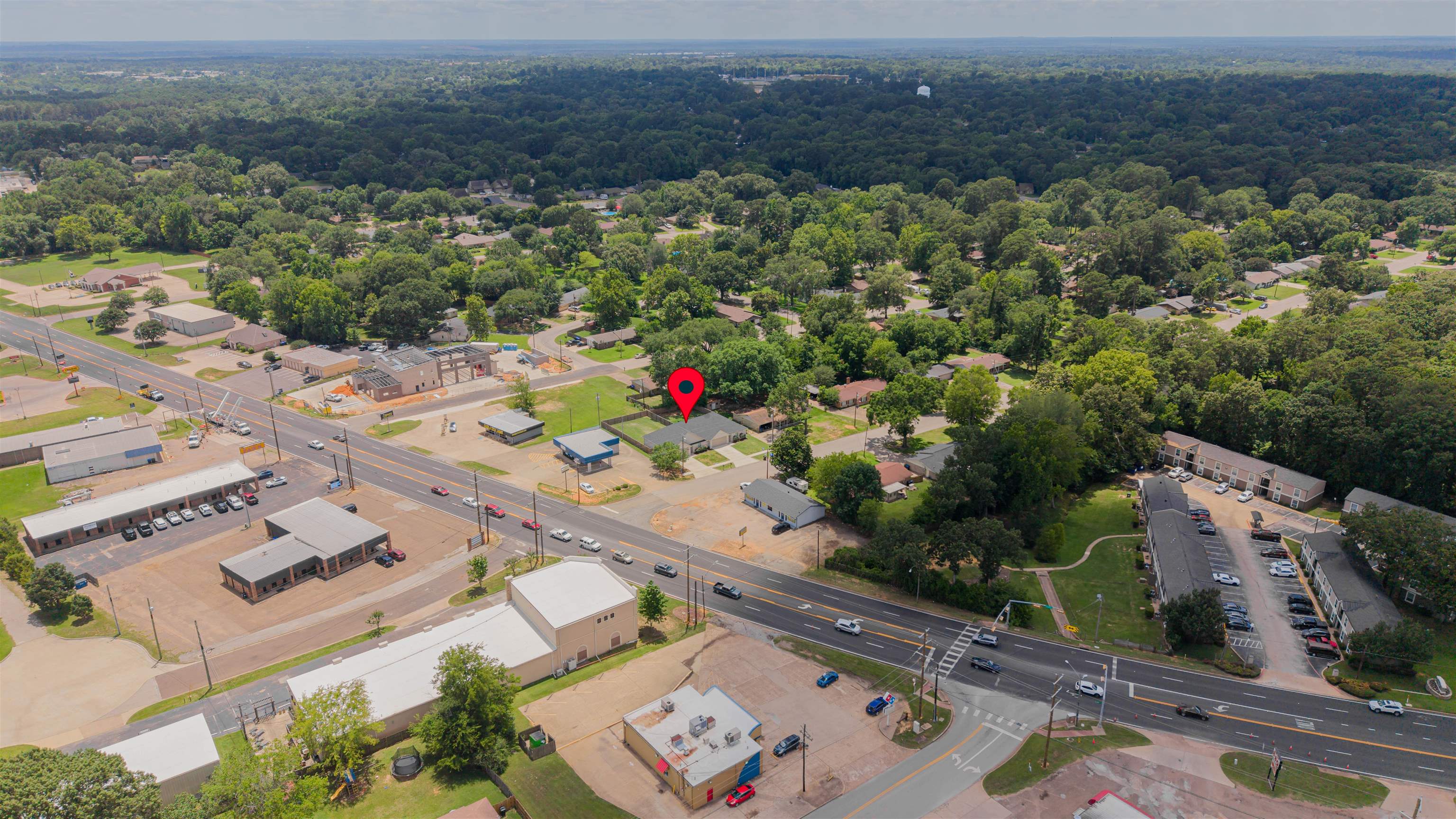 Aerial view of the marked property near a major road, with homes, businesses, and woods nearby.