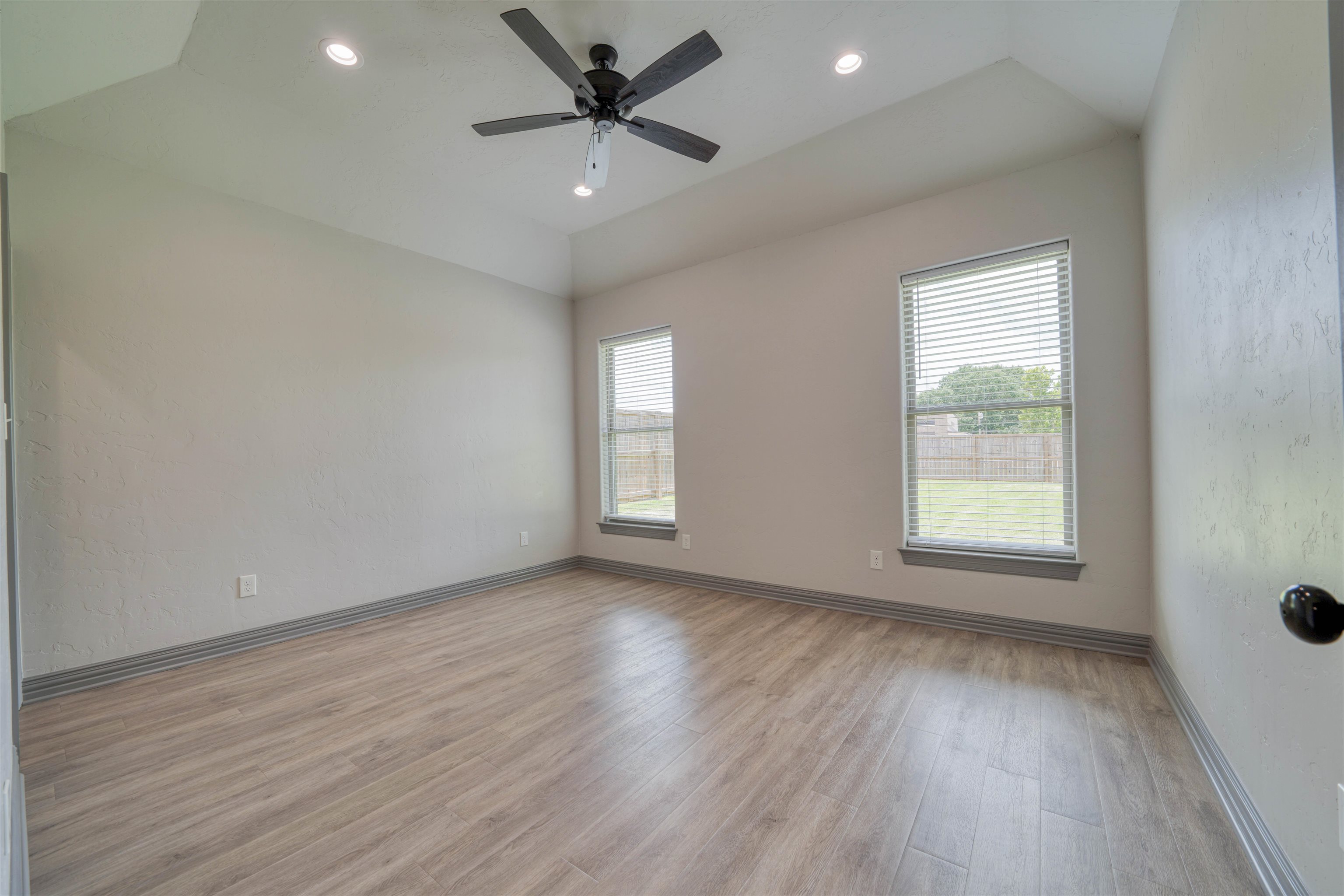 Unfurnished room with wood-look flooring, two windows, and a dark ceiling fan.