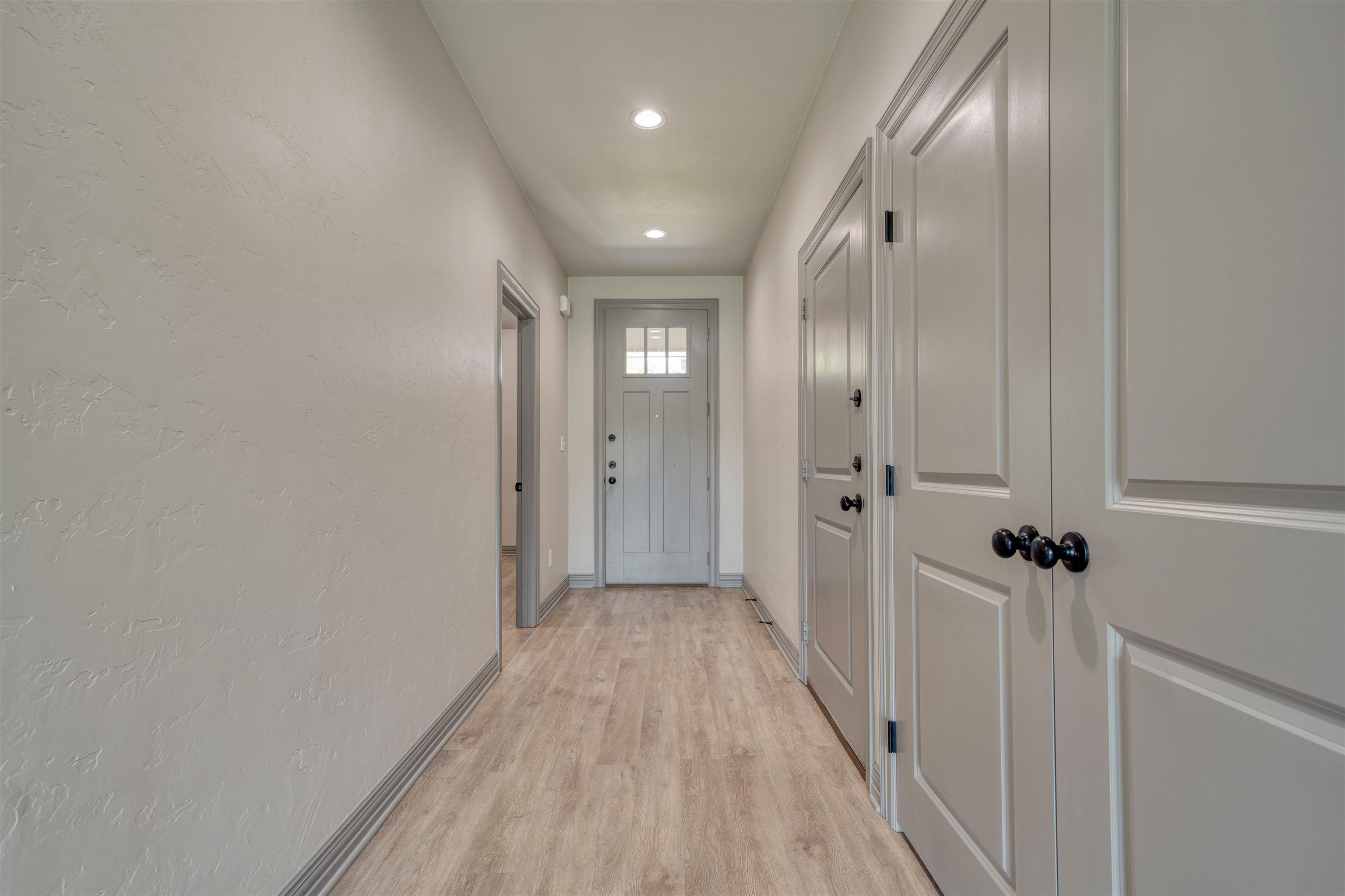Unfurnished hallway with wood-look flooring, paneled doors, and a small window in the entry door.