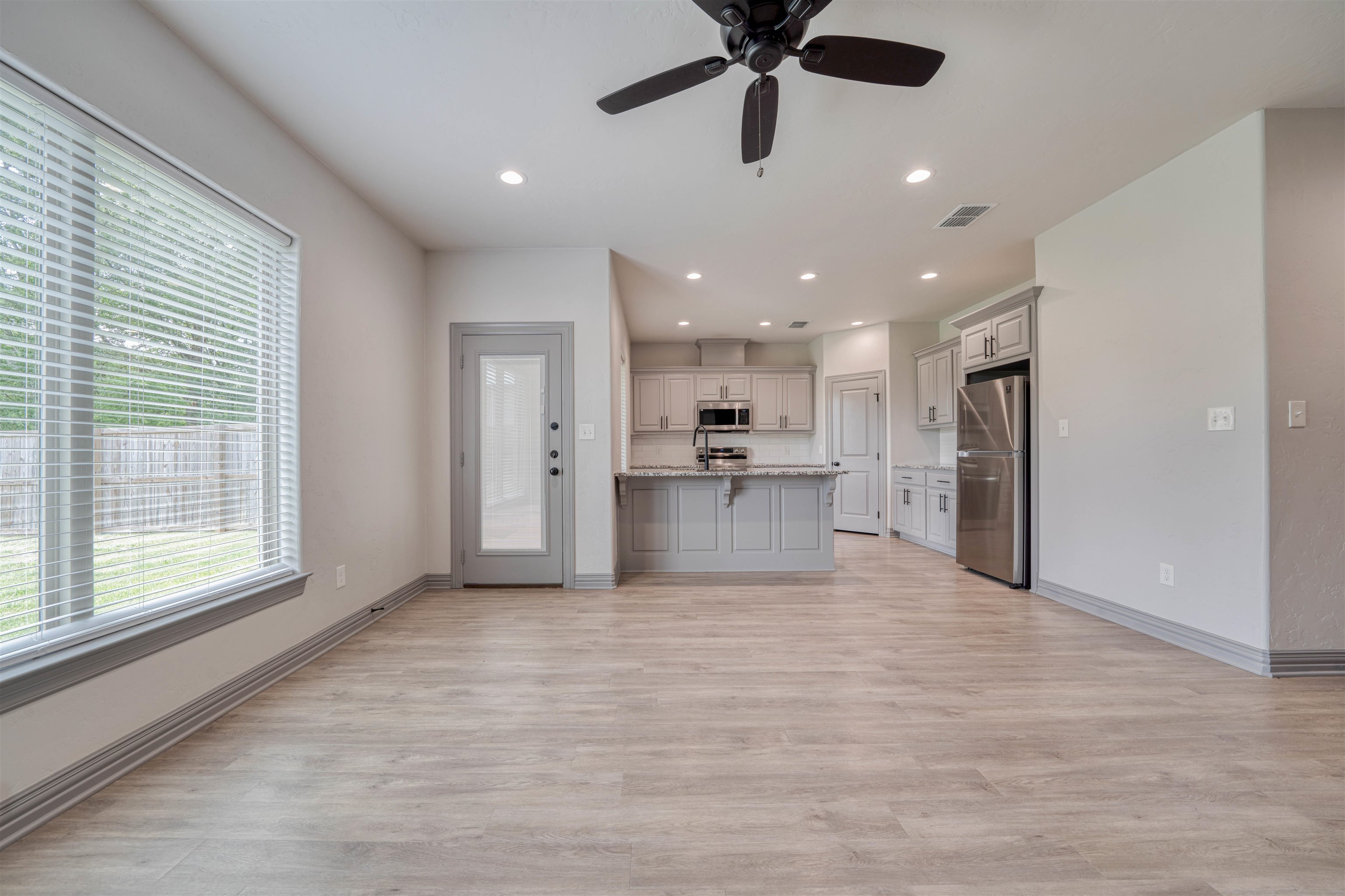 Open-plan living area and kitchen with gray cabinetry, a stone island, and wood-look floors.