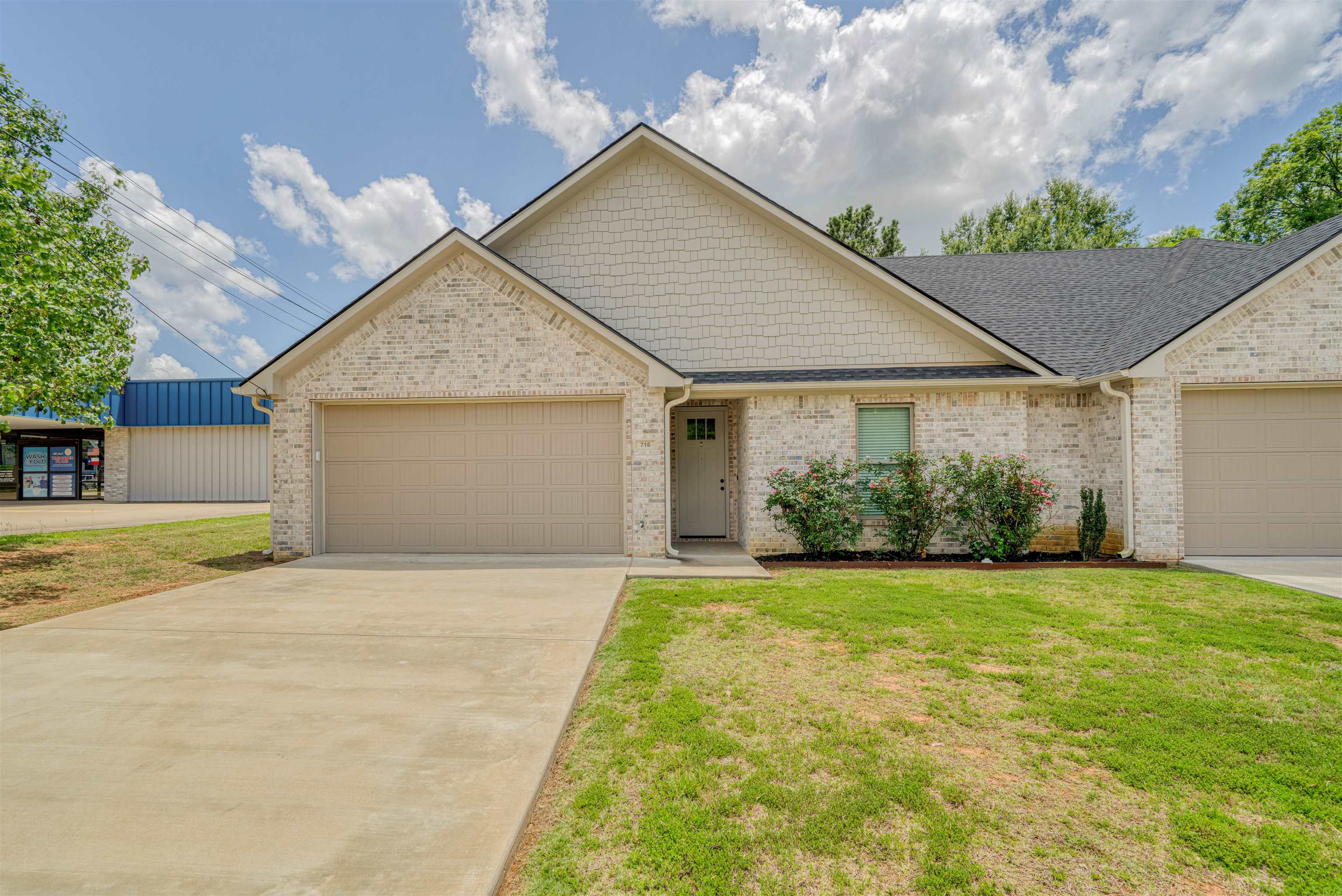 Brick house with cream gables, a two-car garage, landscaped shrubs, and a broad concrete driveway.