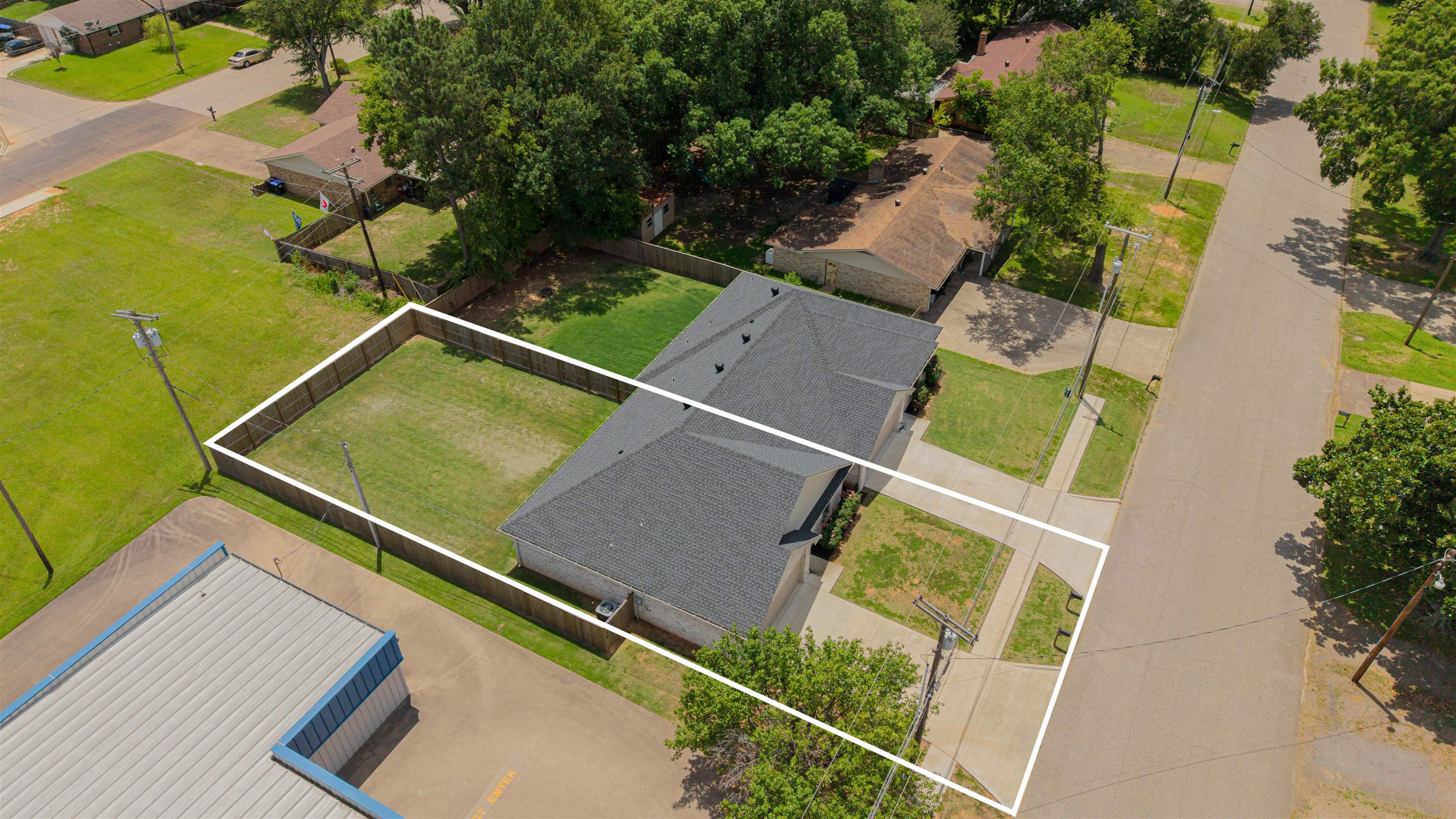 Aerial view of a single-story home and fenced yard outlined along a residential street.