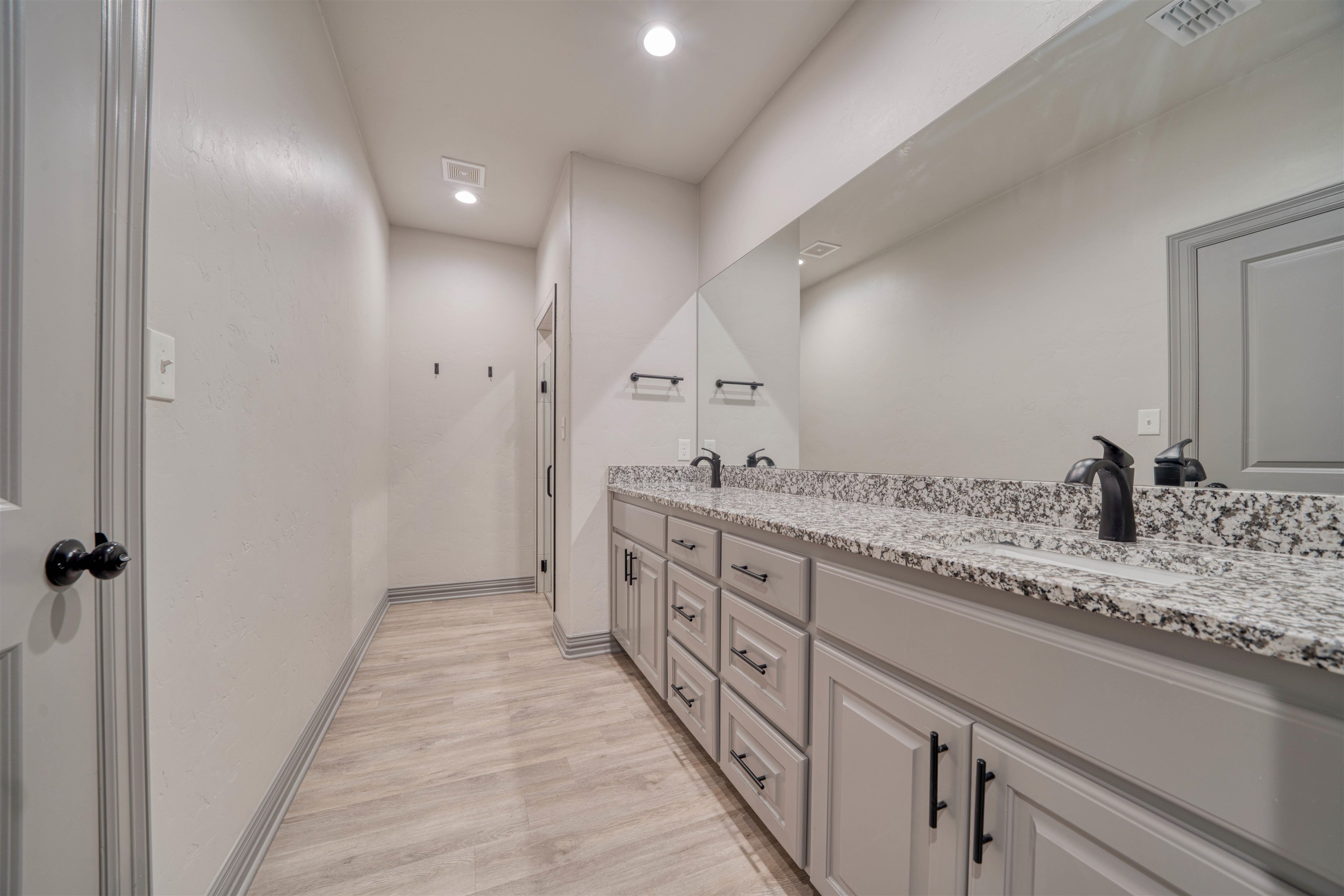 Long bathroom vanity with speckled granite countertop, dark faucets, and a large mirror.