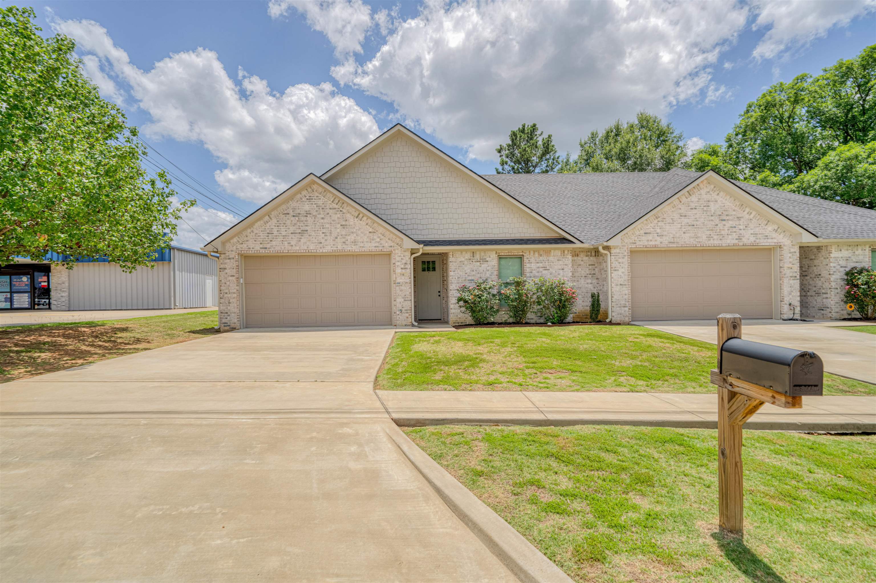 Brick duplex with two garage doors, central entrance, broad concrete driveways, and a mailbox by the lawn.