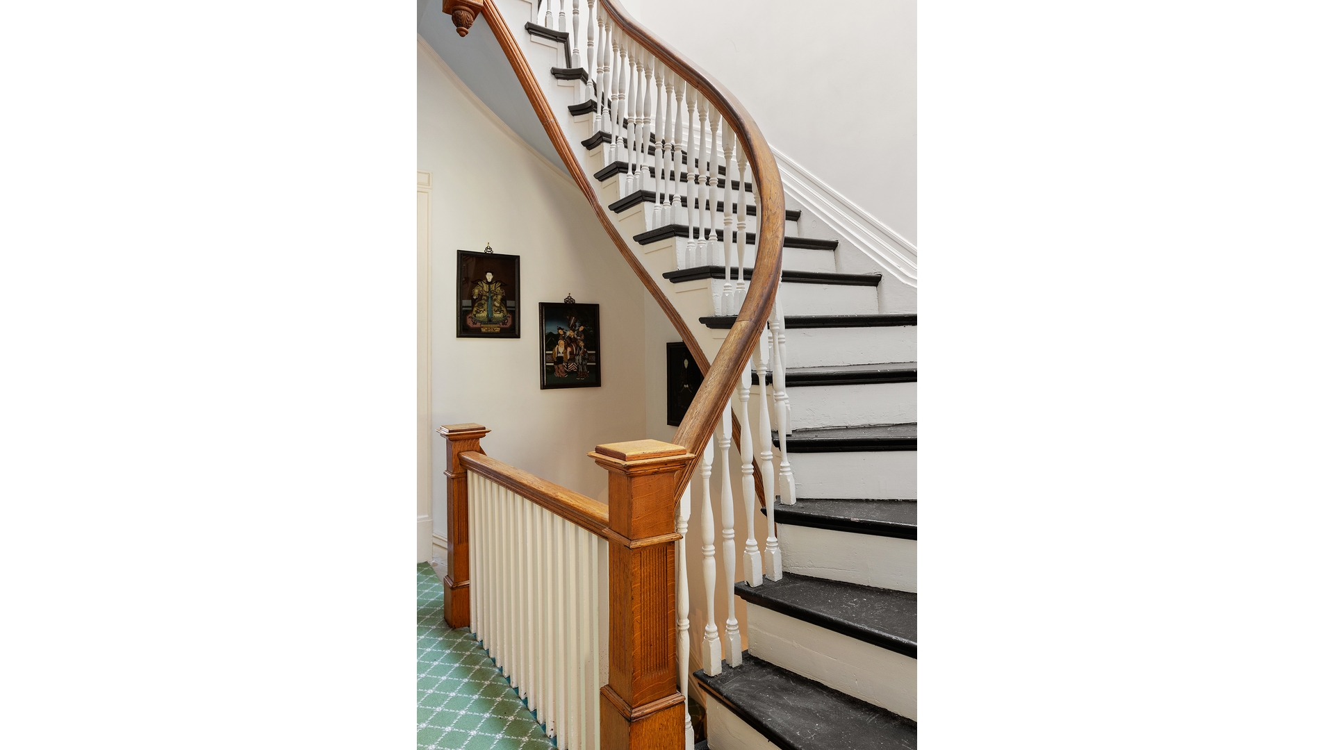 Curved staircase with a polished wood handrail, white balusters, black treads, and green patterned carpet.