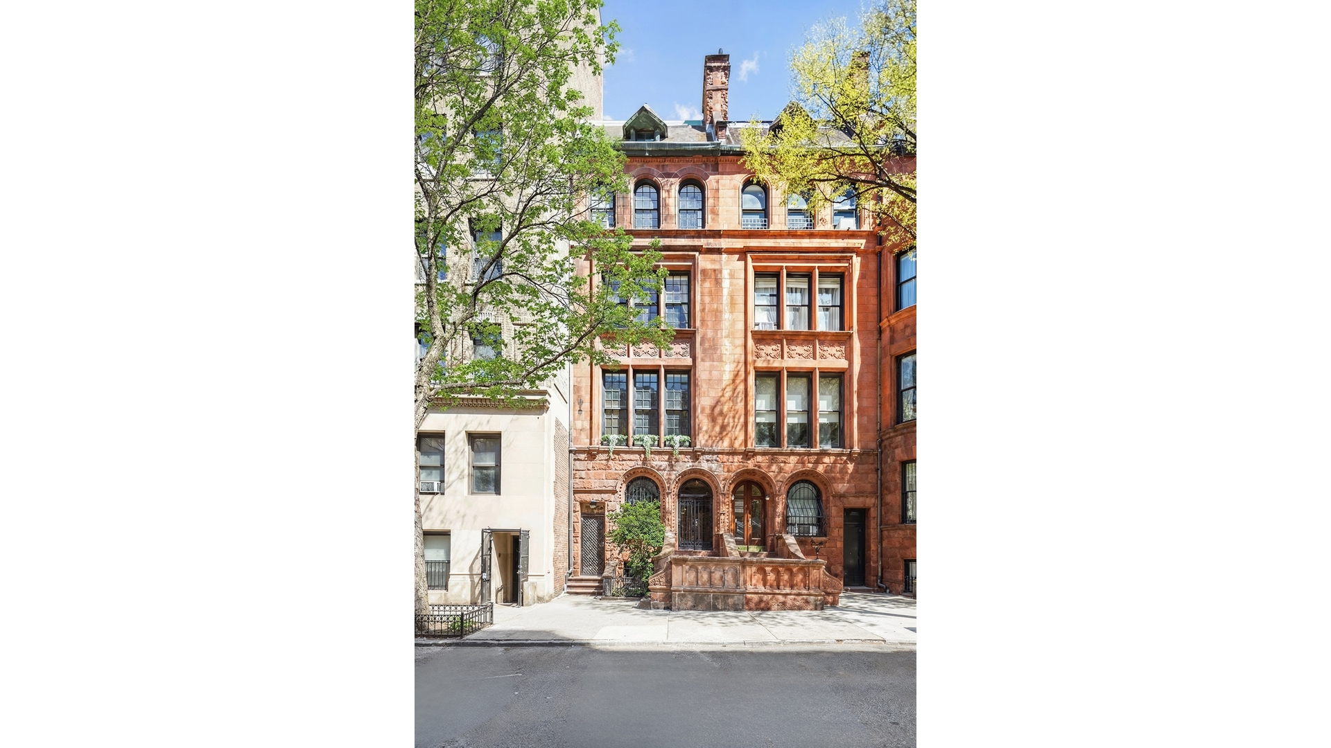 Red-brownstone townhouse with ornate arched windows and a raised stoop, framed by leafy trees.