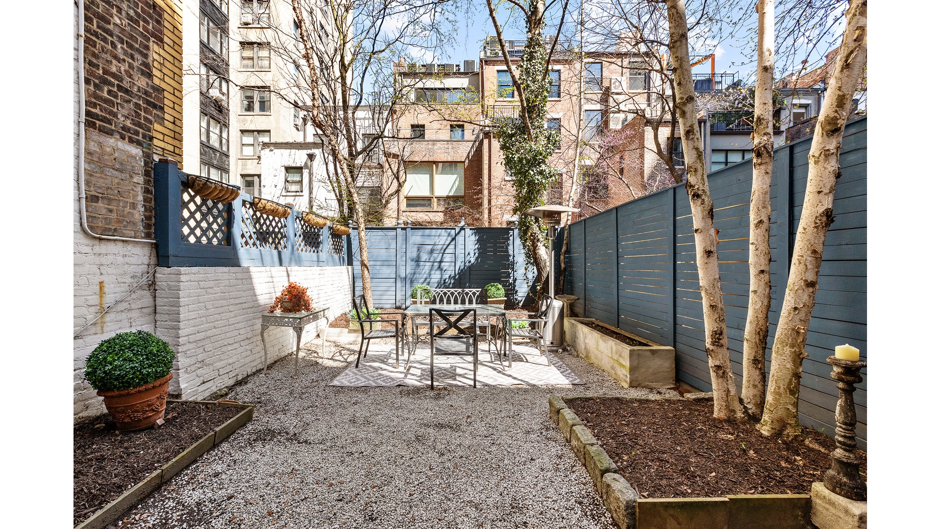Private courtyard patio with gravel, outdoor dining set, tall blue fencing, and trees.
