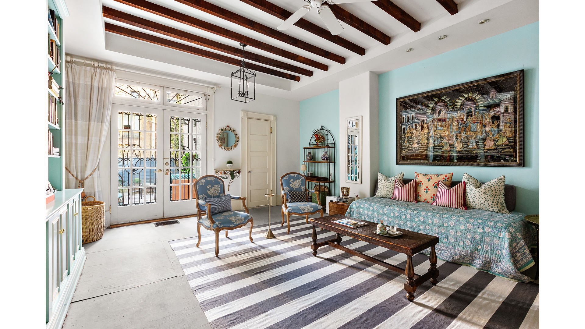 Living room with exposed wood beams, French doors, a teal wall, and a patterned daybed.