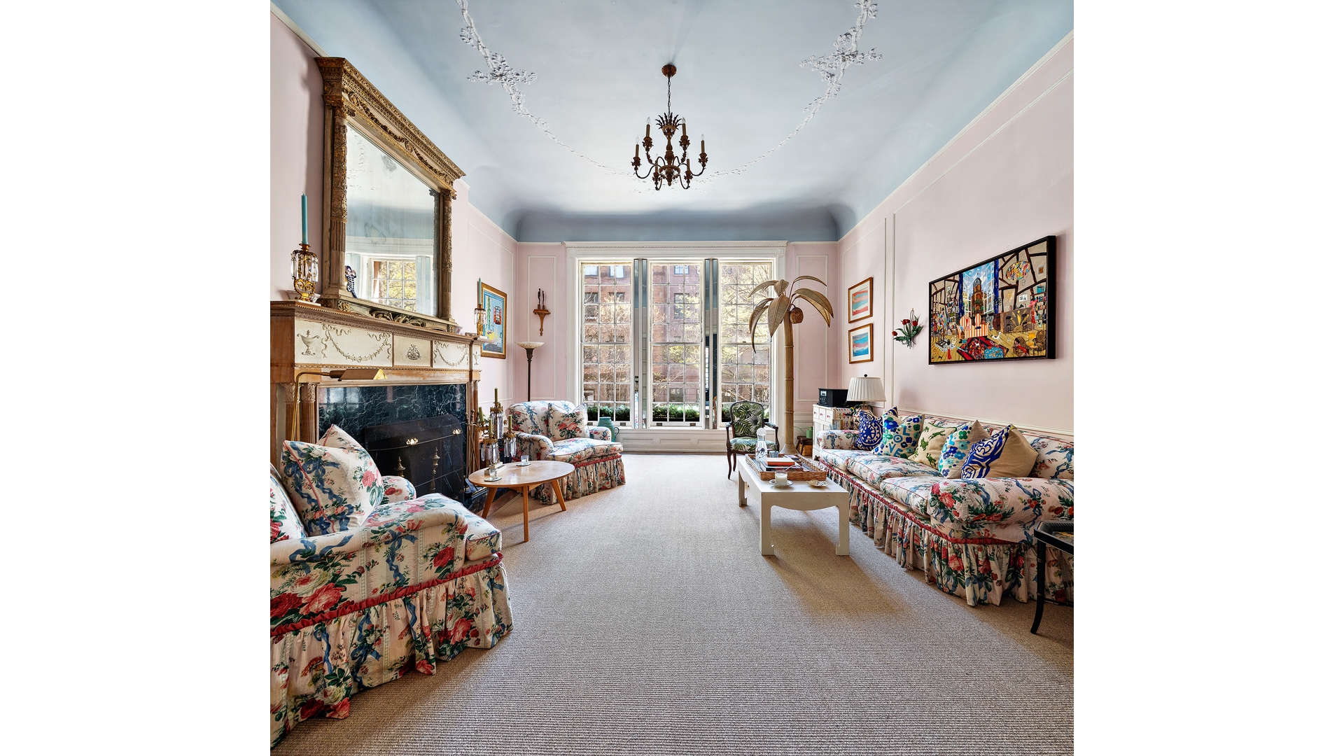 Living room with a decorative fireplace, tall windows, chandelier, and floral-patterned seating.
