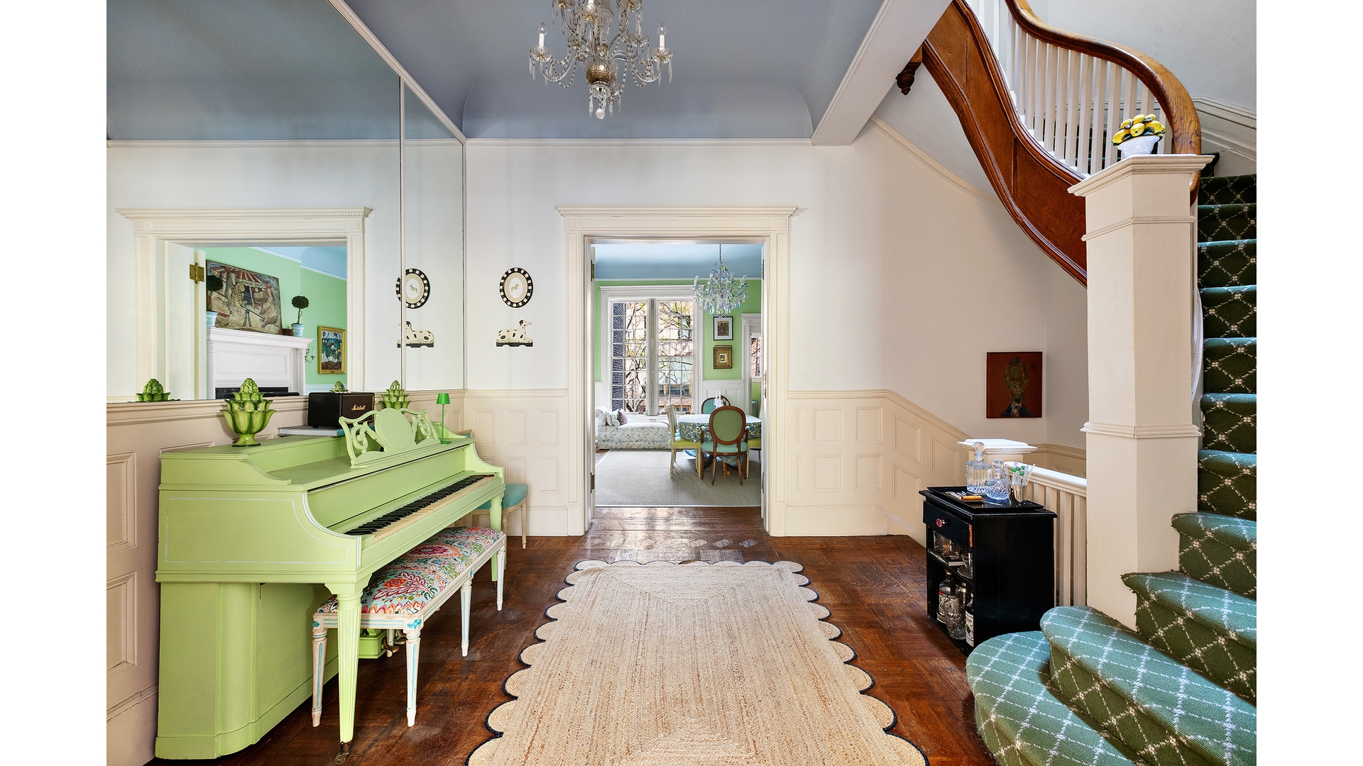 Entry hall with a pale green piano and curved staircase with green carpeted steps.