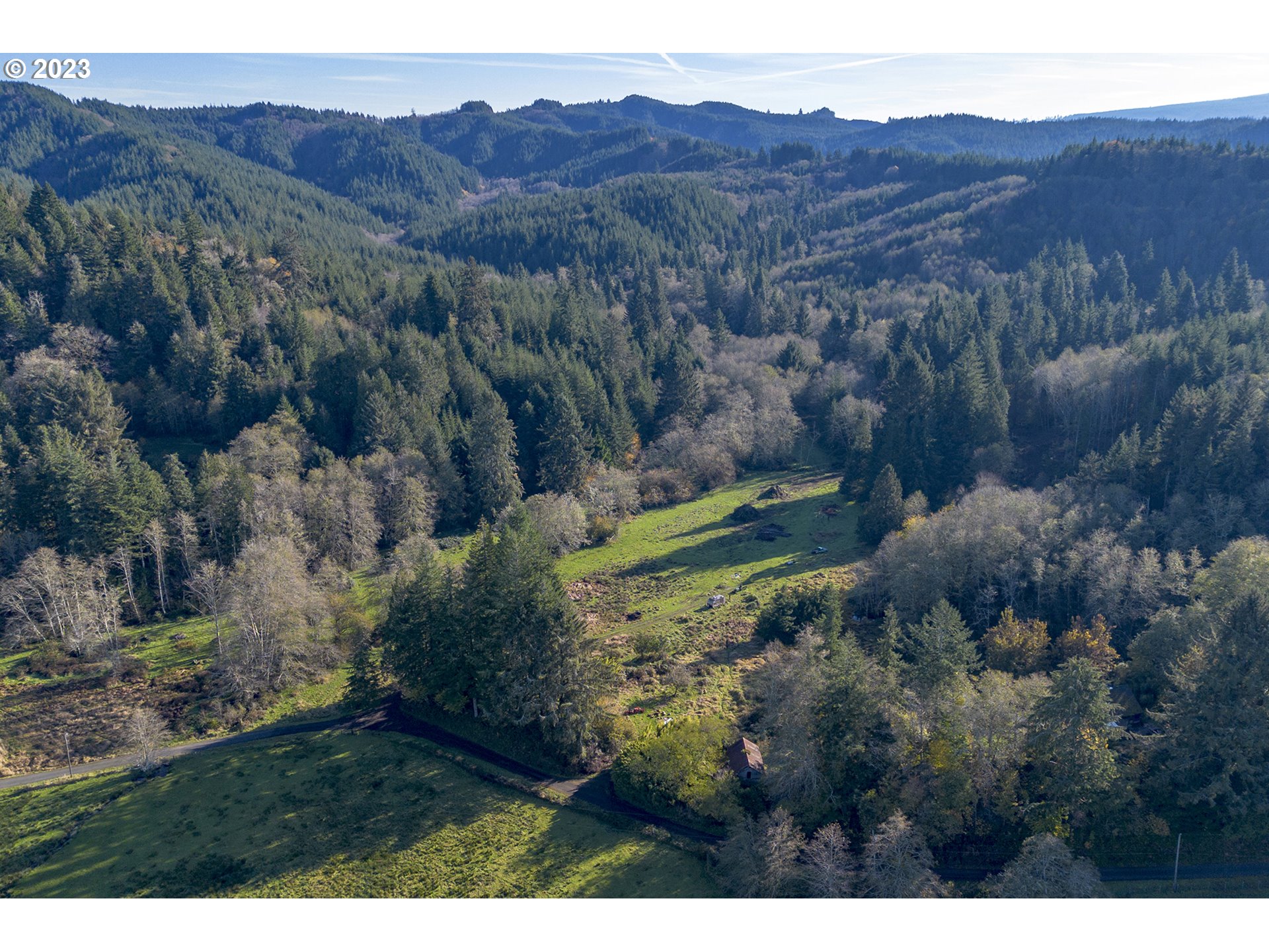 Aerial view of a grassy clearing and small outbuilding surrounded by forest and wooded hills.