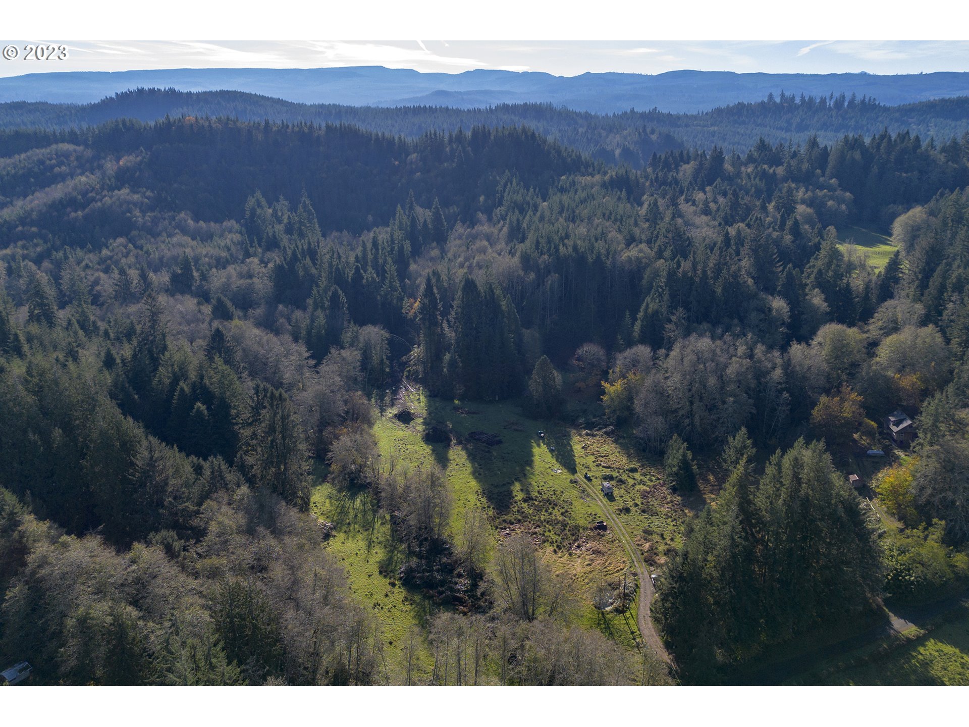 Aerial view of a wooded property with a central grassy clearing and surrounding hills.