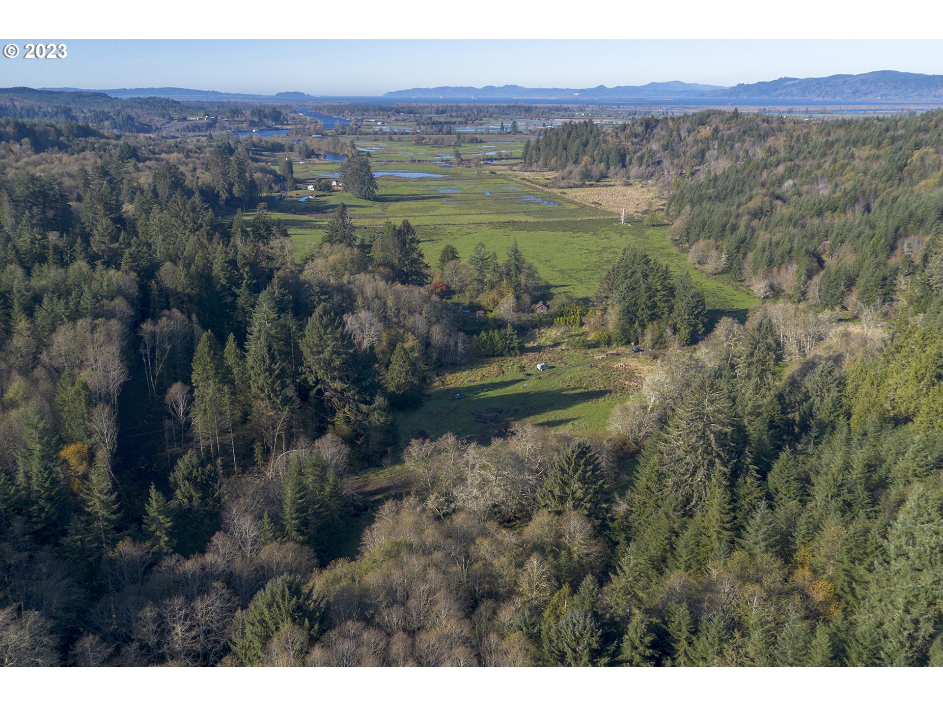 Aerial view of wooded acreage and open fields with wetland channels and distant hills.