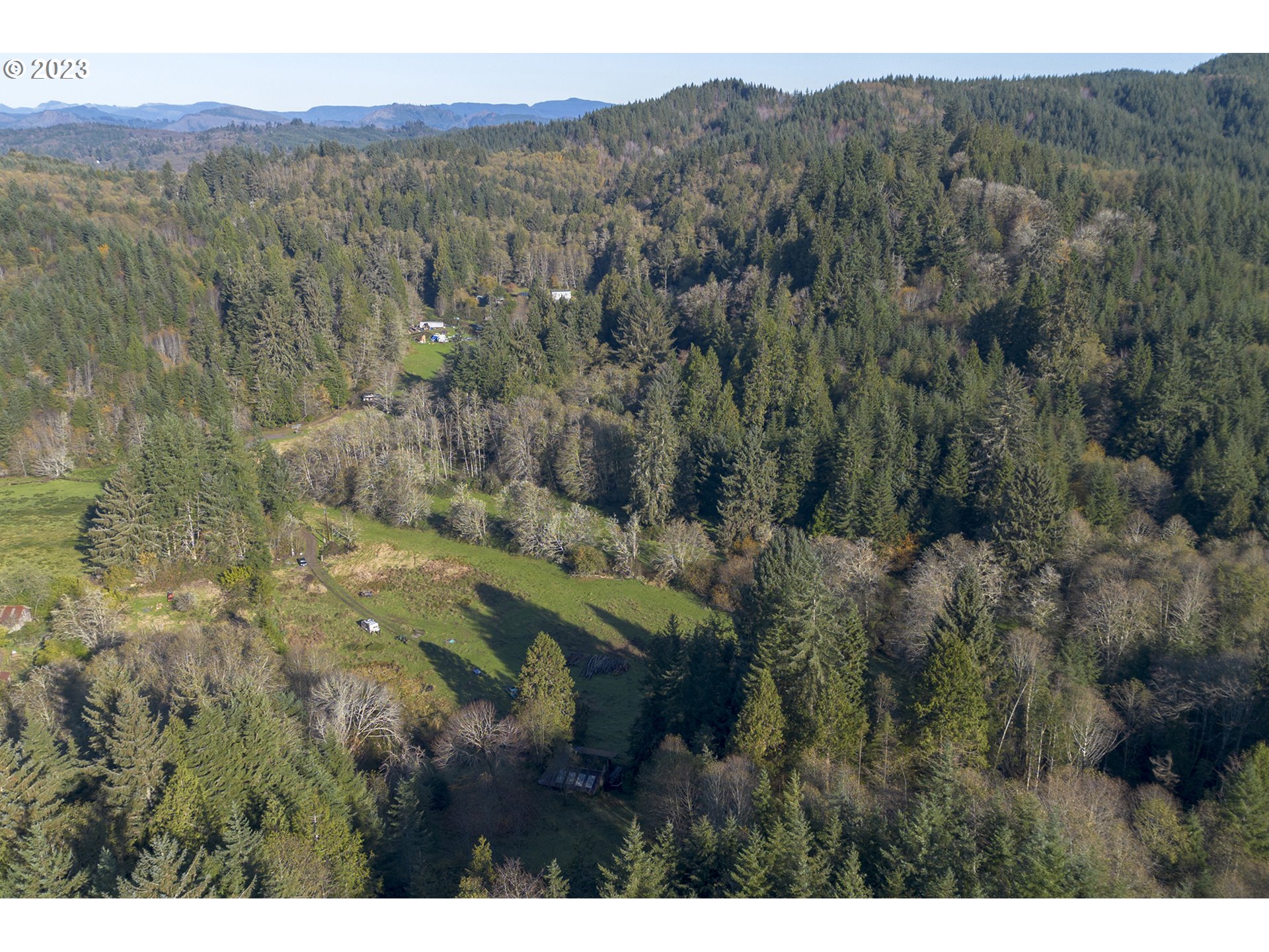 Aerial view of a forested rural property with grassy clearings, a winding driveway, and scattered buildings.