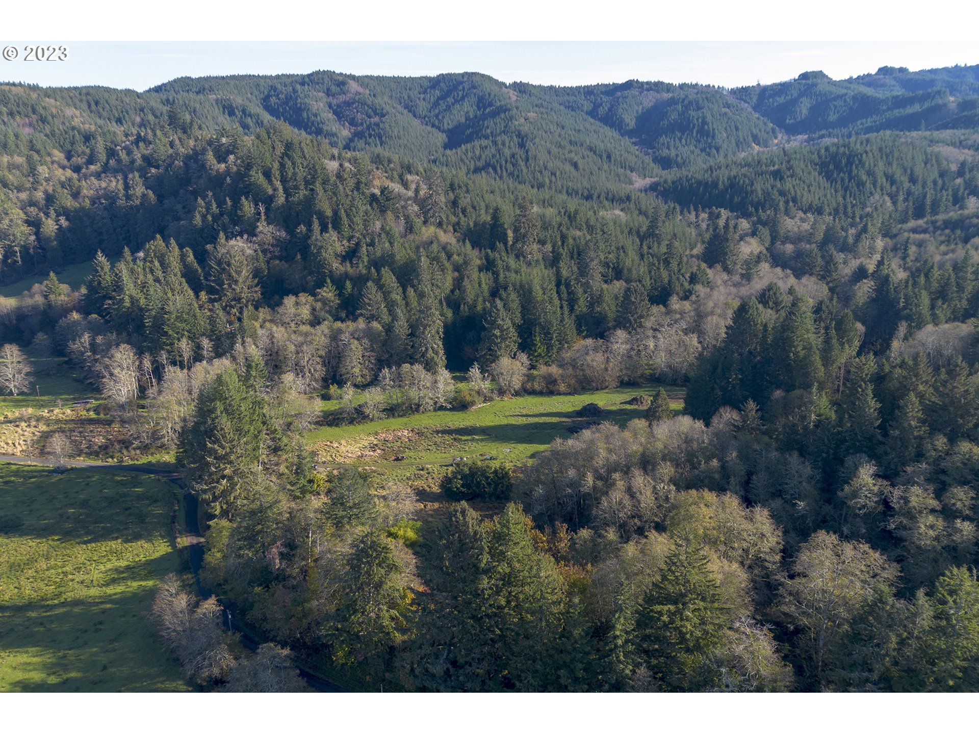 Aerial view of grassy fields and woodland bordered by forested hills.