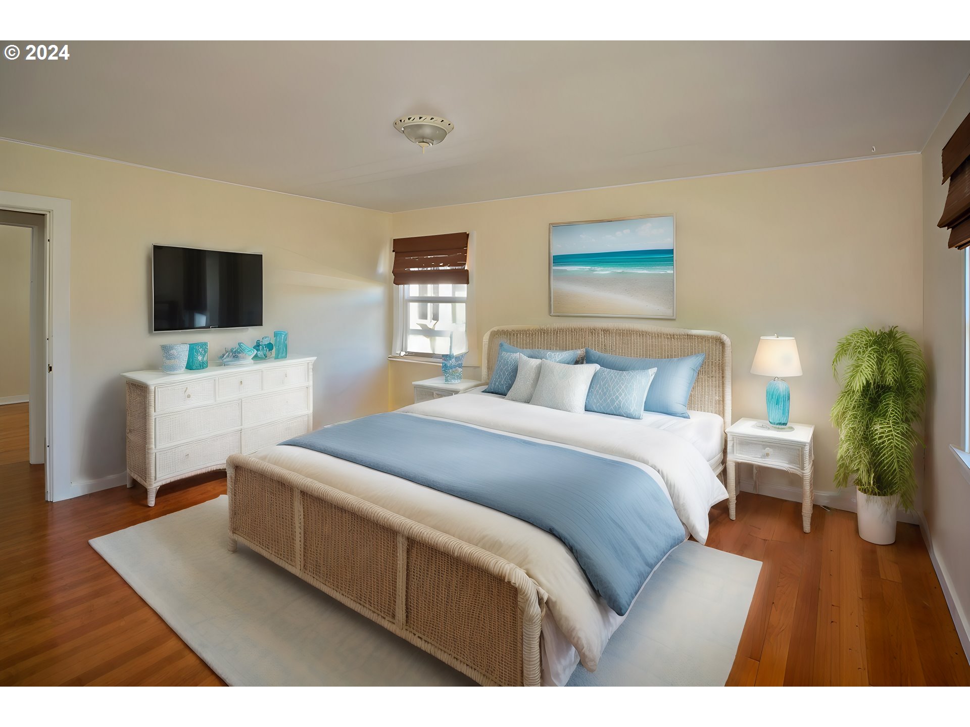 Bedroom with a woven bed, pale blue bedding, hardwood floors, and a potted palm.