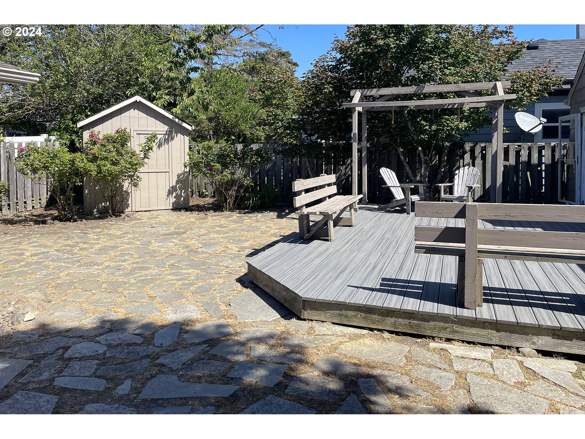 Backyard patio with a raised deck, pergola, outdoor chairs, stone paving, and a garden shed.