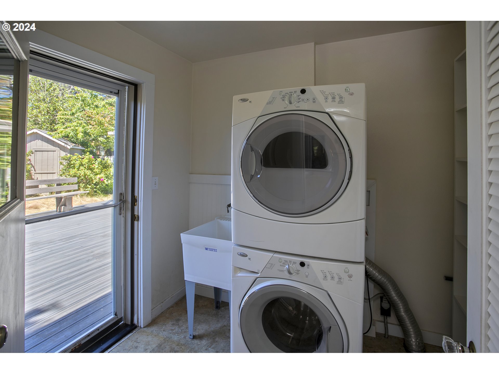 Laundry room with stacked washer and dryer beside a utility sink and deck door.
