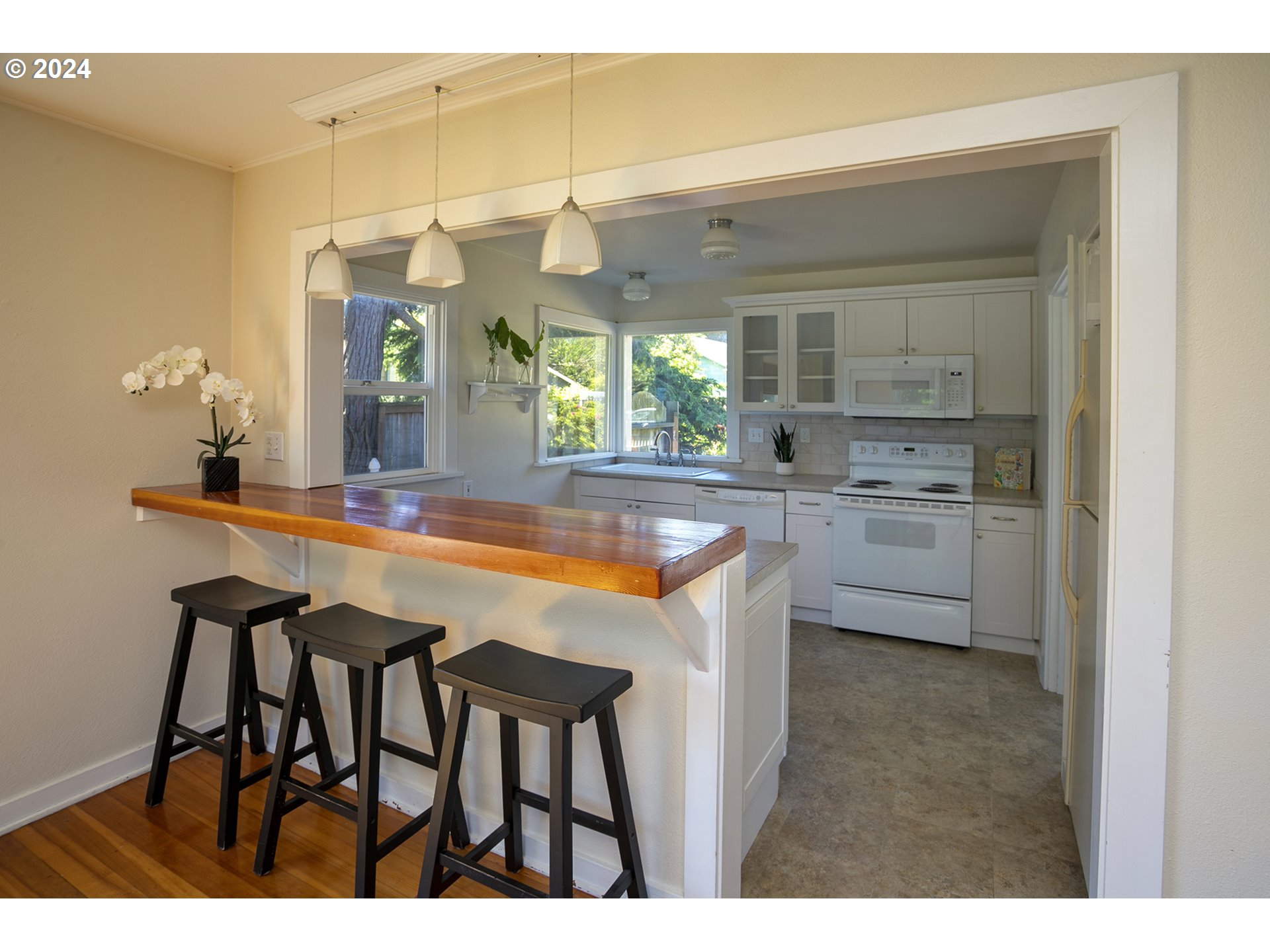 Kitchen with white cabinets, window-side sink, and a wooden breakfast bar with three stools.