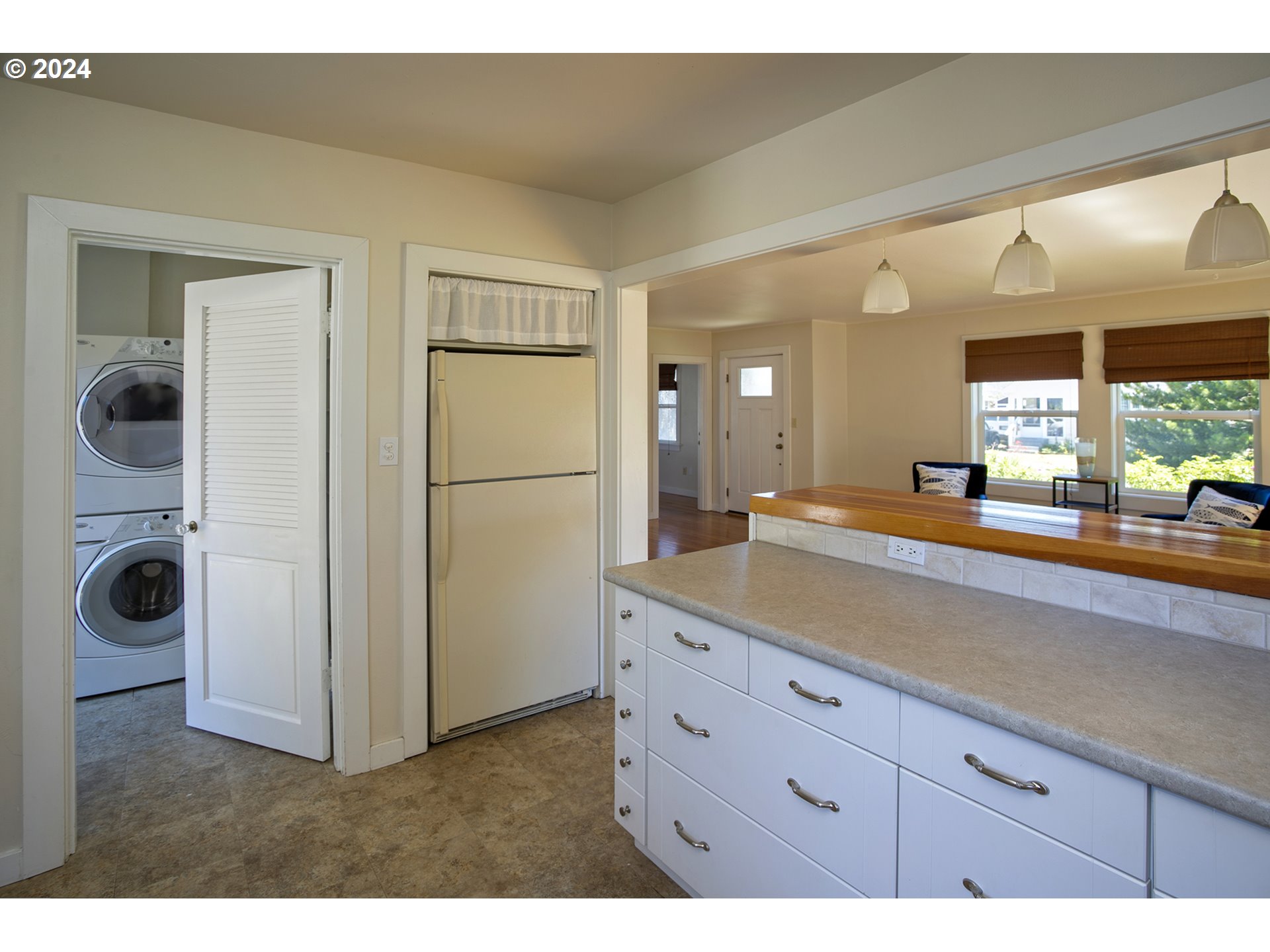 Kitchen with a large island, refrigerator, and open laundry closet with stacked washer and dryer.