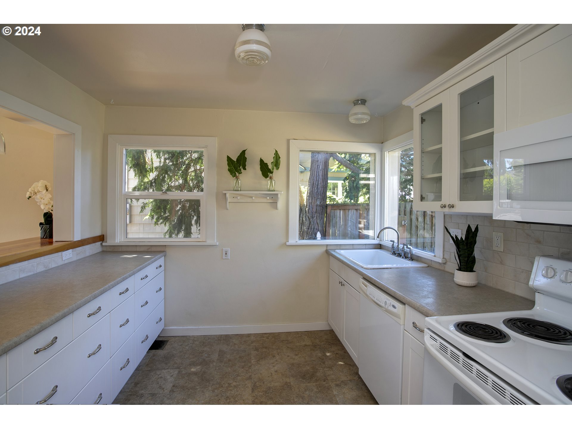 Kitchen with white cabinets and gray counters, featuring a corner sink beneath wide windows.