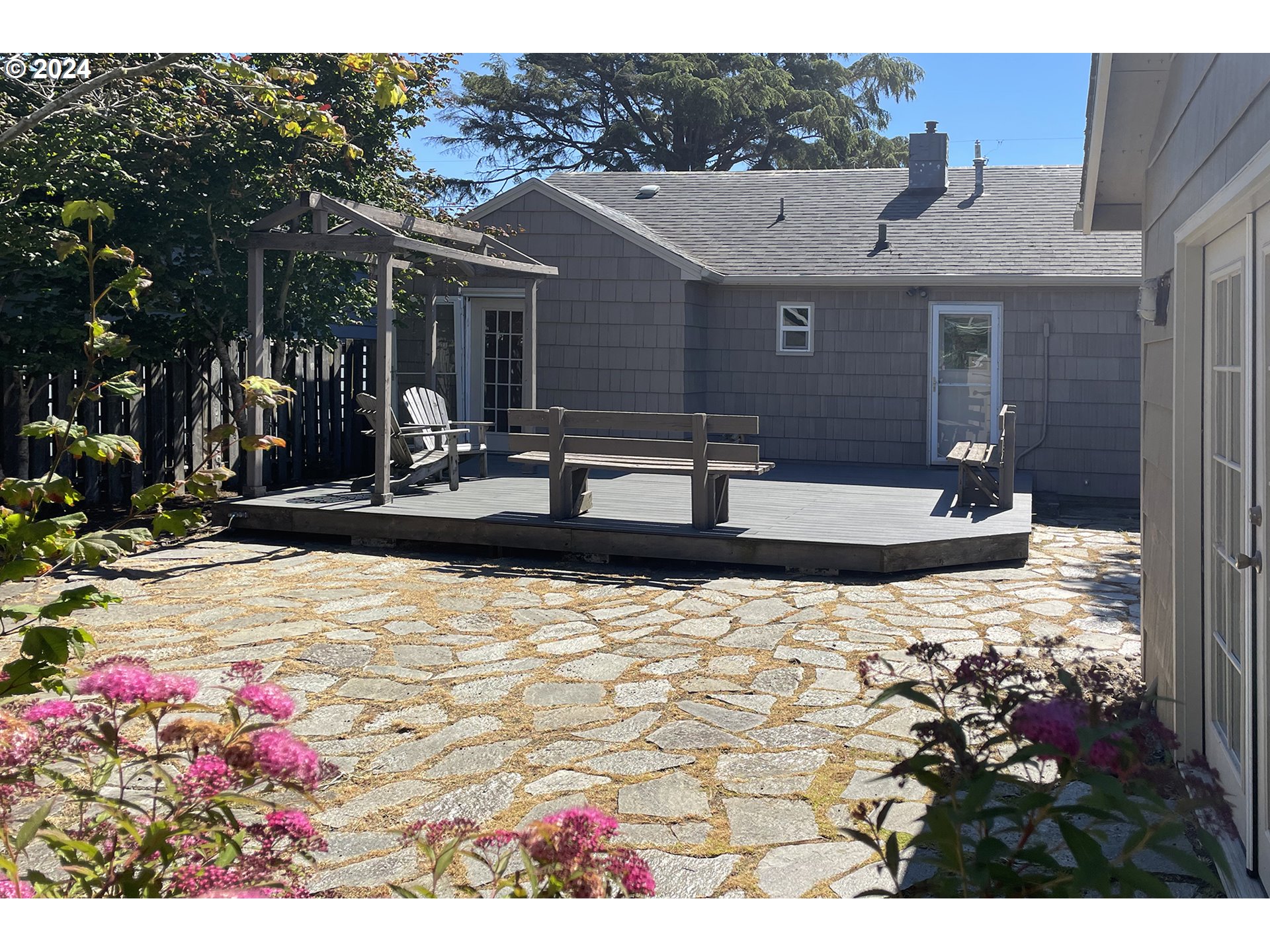 Back patio with a raised deck, pergola, outdoor seating, and a broad stone-paved courtyard.