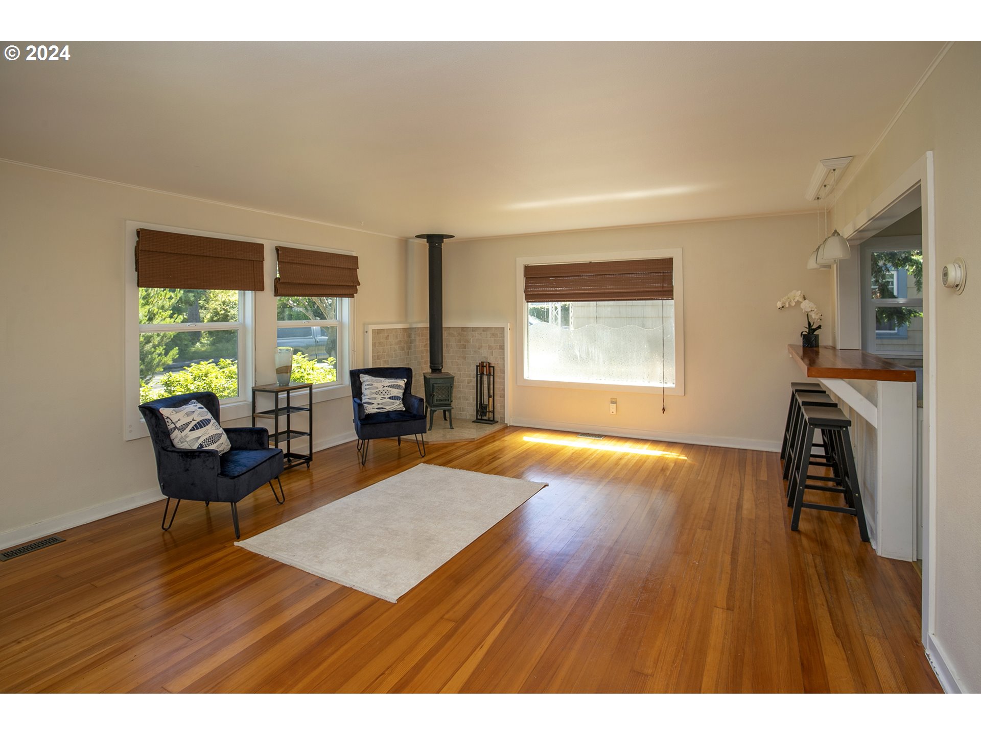 Living room with hardwood floors, a wood stove, large windows, and bar seating.