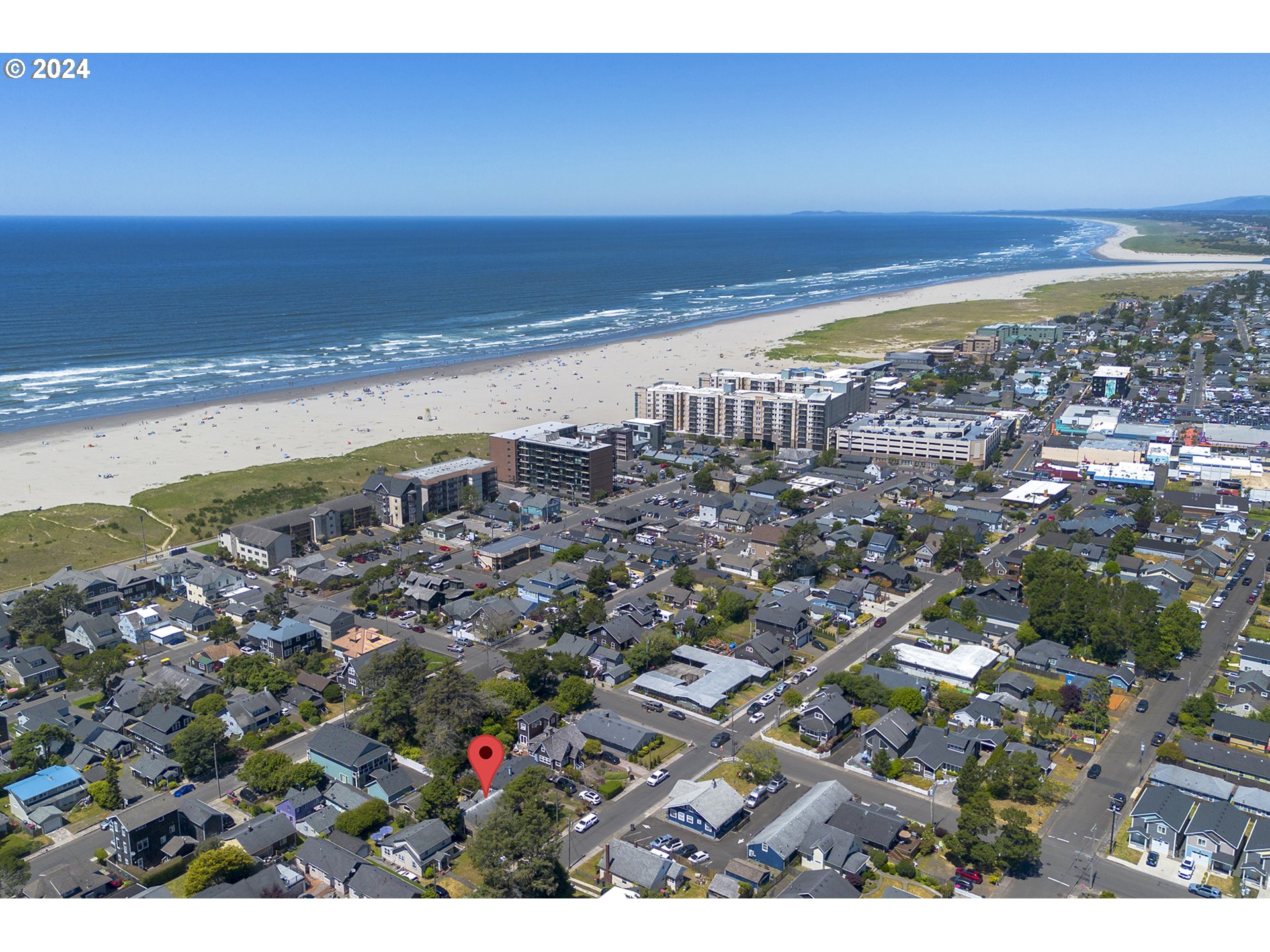 Aerial view of a Seaside neighborhood, with the beach and Pacific Ocean beyond and a red pin marking a property.