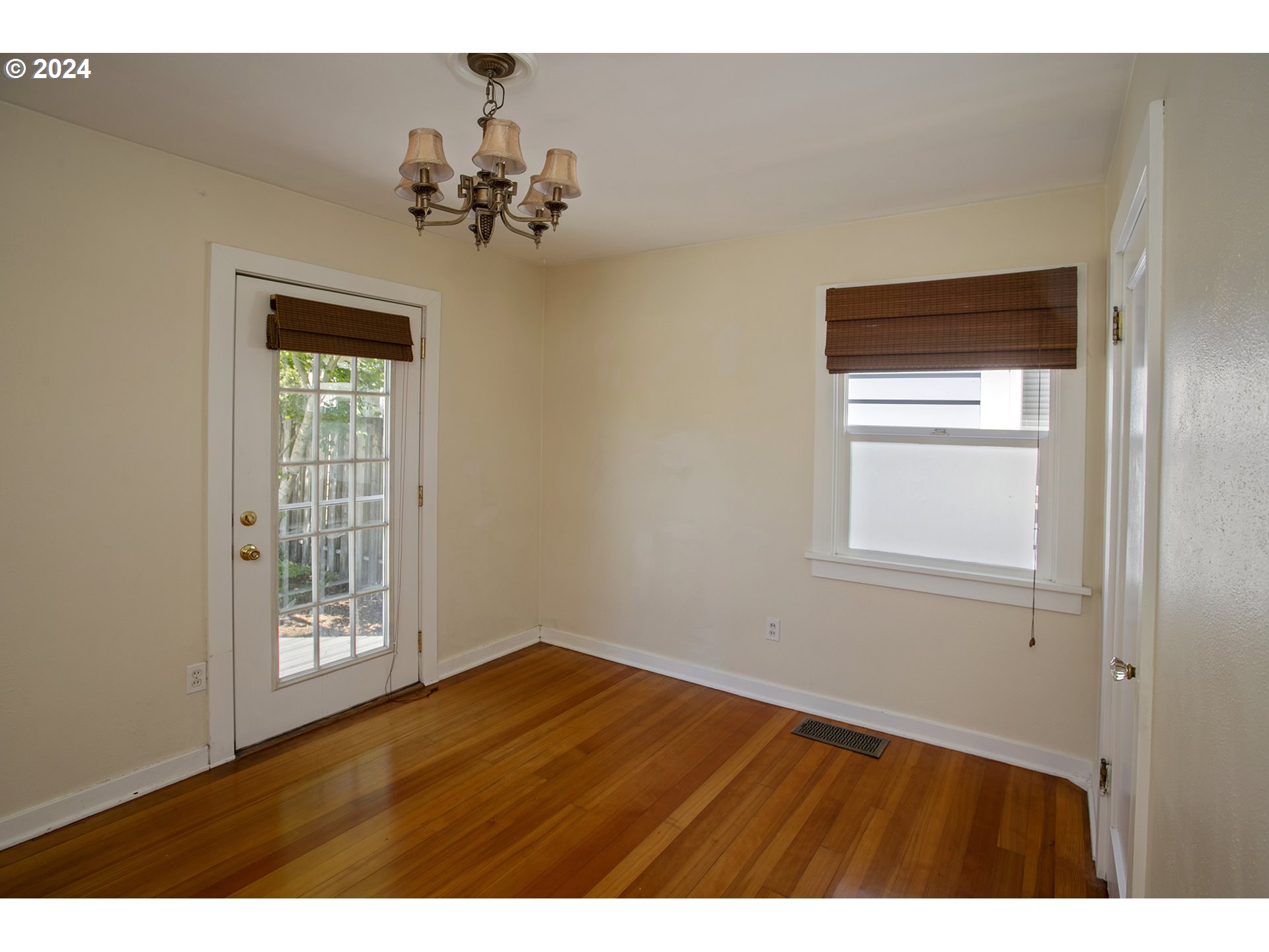 Empty room with hardwood floors, a glass-paneled door, window, and chandelier.