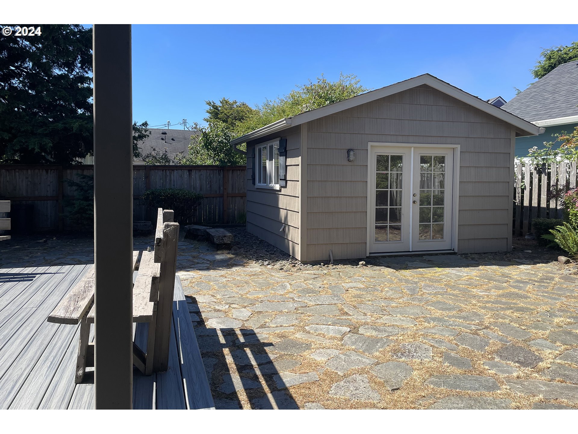 Backyard shed with white French doors beside a stone patio and wooden deck.