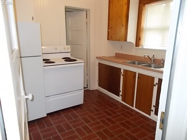 Kitchen with a white electric range, wood-tone cabinets, and reddish-brown tile flooring.