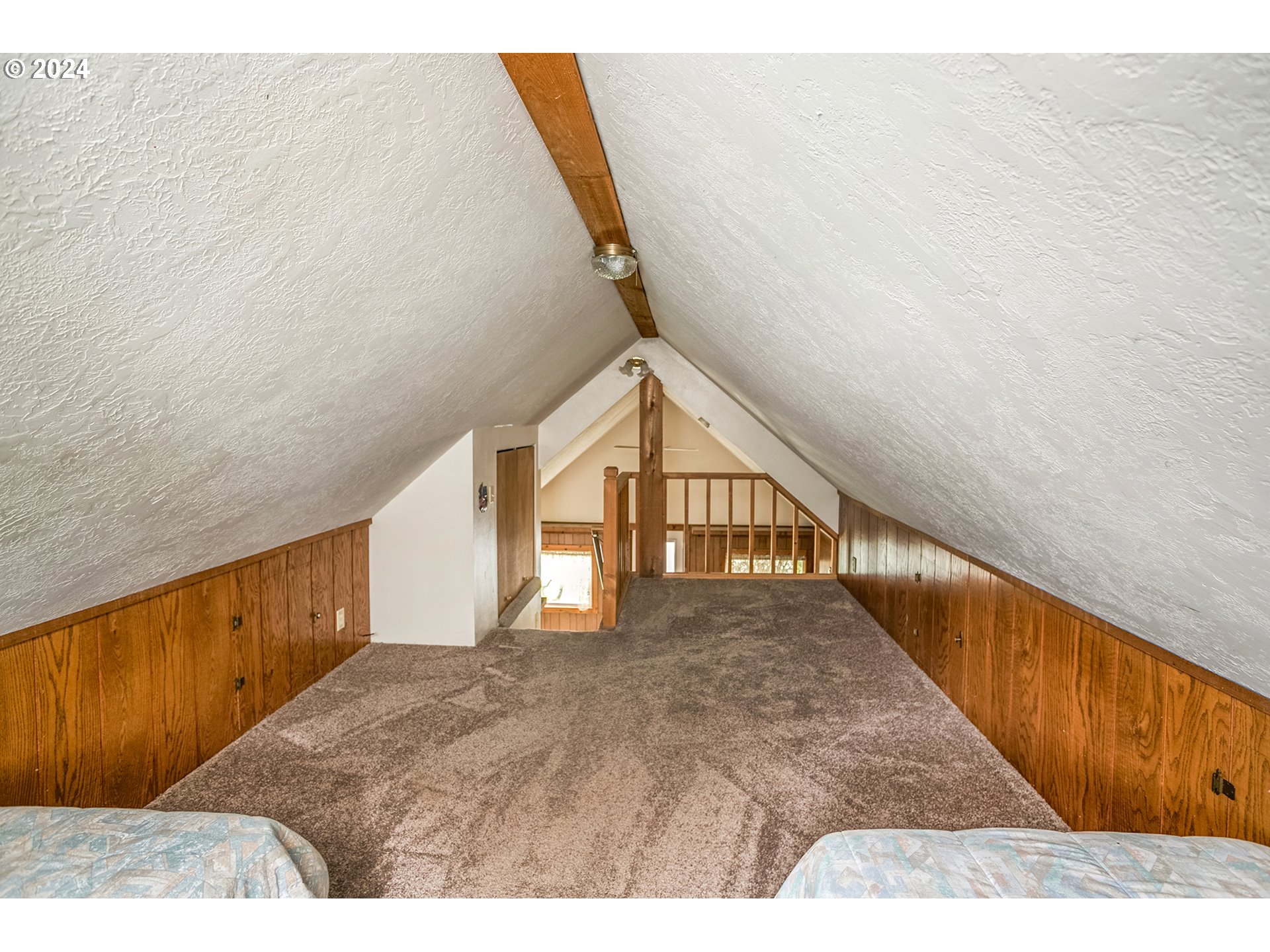 Attic bedroom with a vaulted ceiling, wood paneling, carpet, and railing overlooking the level below.