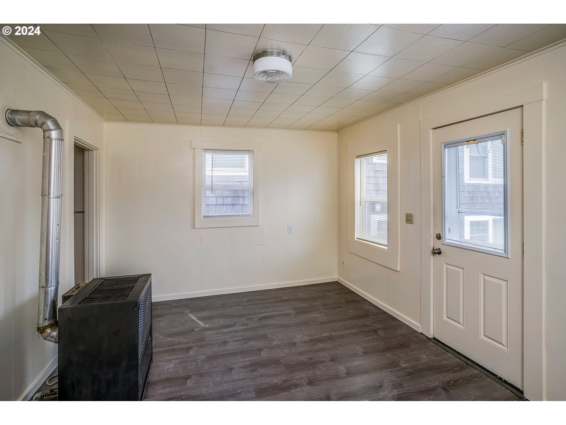 Vacant room with dark flooring, two windows, a glazed door, and a black heating unit.