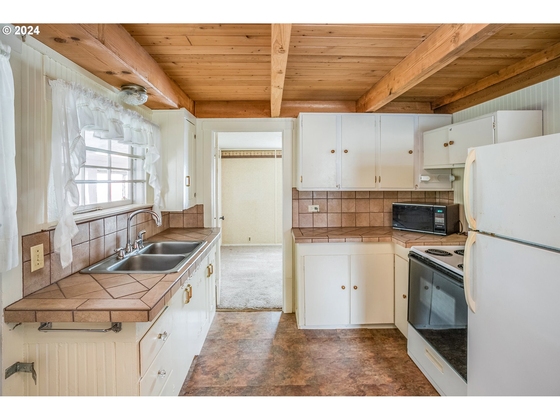 Kitchen with brown tile counters, white cabinets, and an exposed wood-beam ceiling.