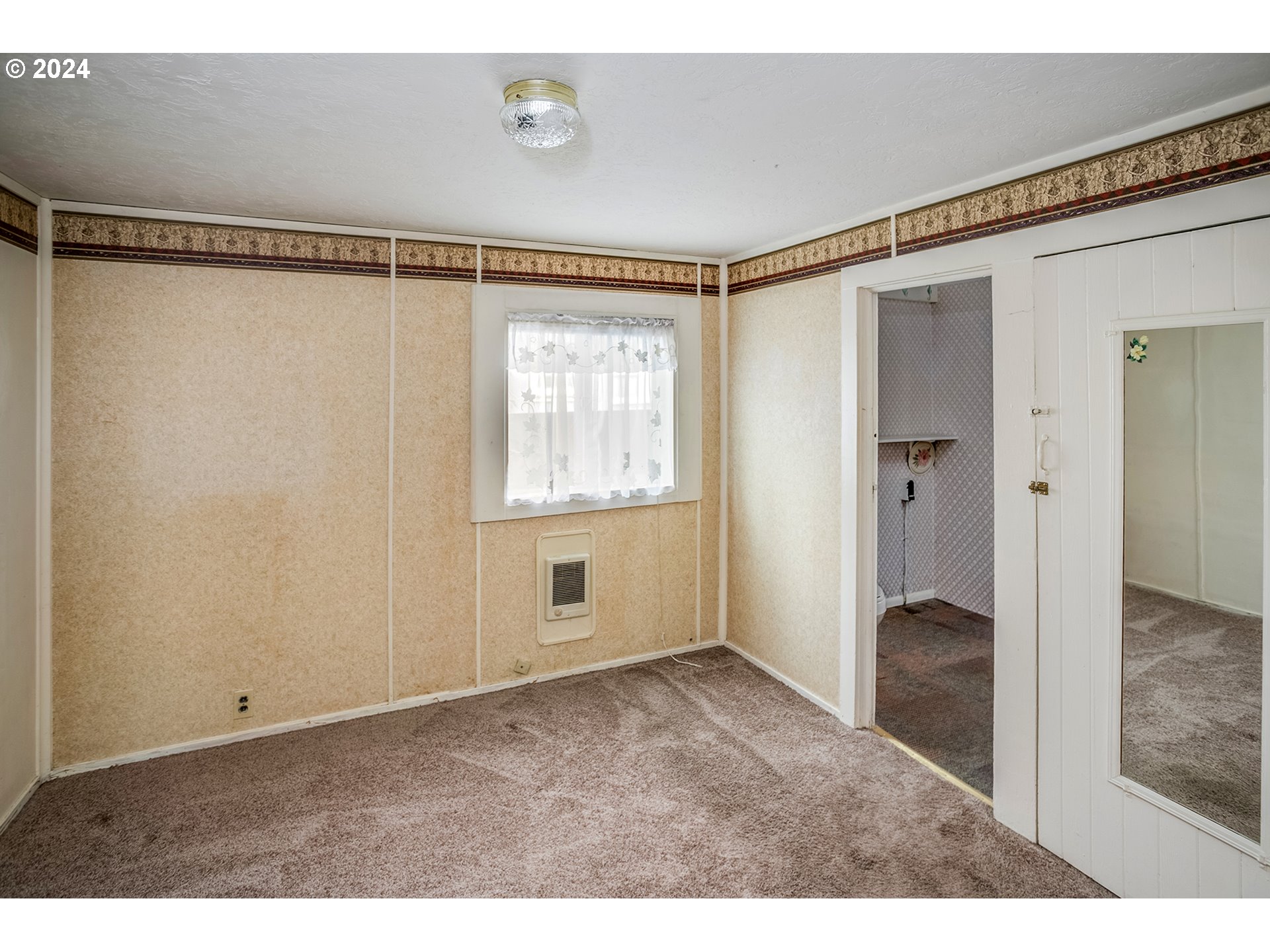 Unfurnished bedroom with beige patterned walls, a curtained window, and carpeted floor.