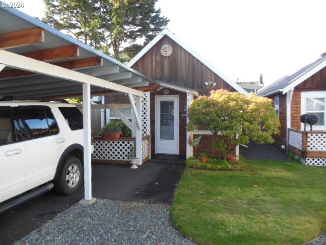 House with a covered carport, white SUV, gabled entrance, lattice railing, and front lawn.