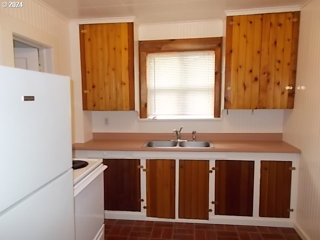 Kitchen with wood-paneled cabinets, a double sink beneath a window, and white appliances.