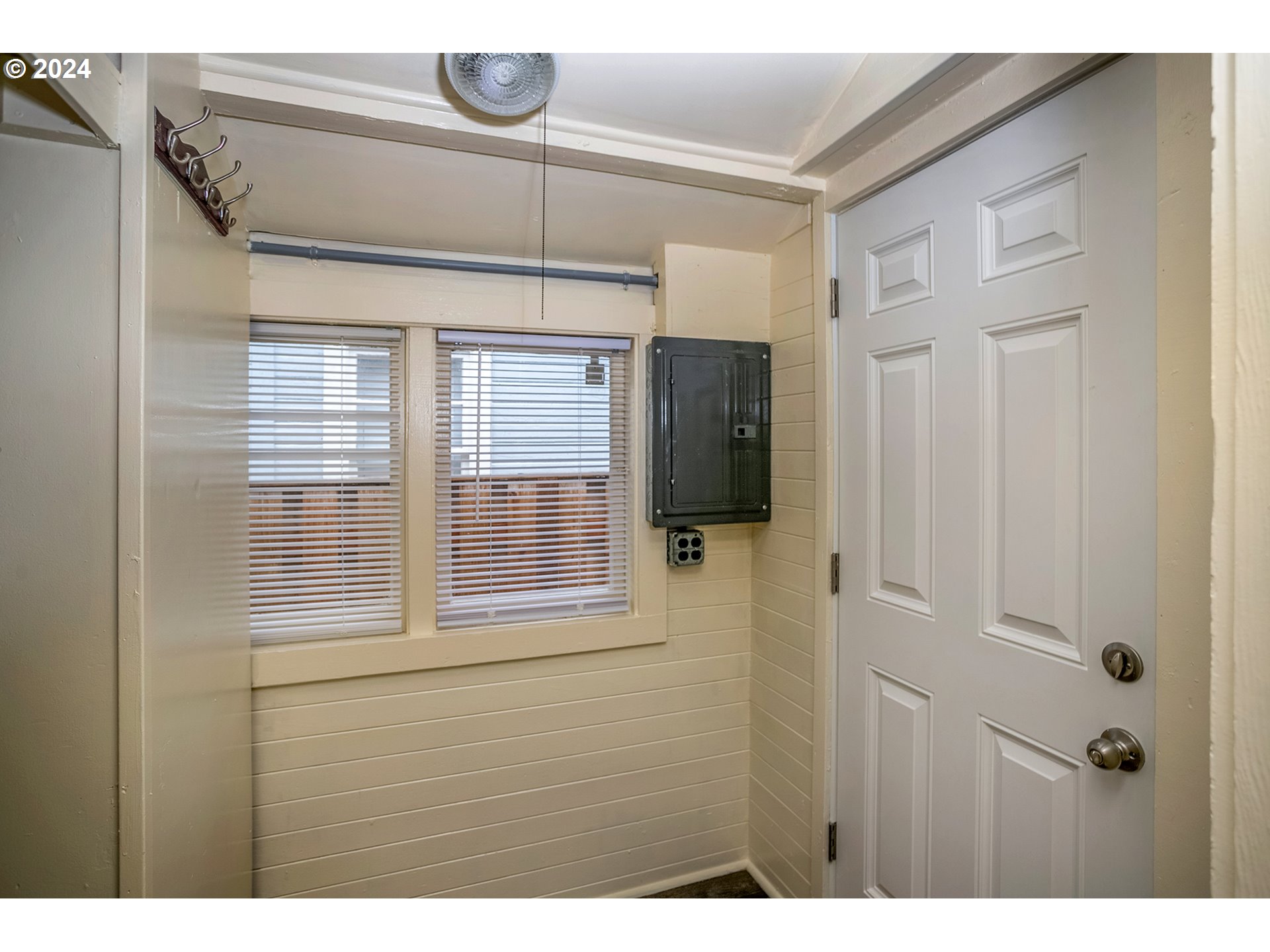 Entryway with two blinded windows, wall-mounted coat hooks, an electrical panel, and a white door.