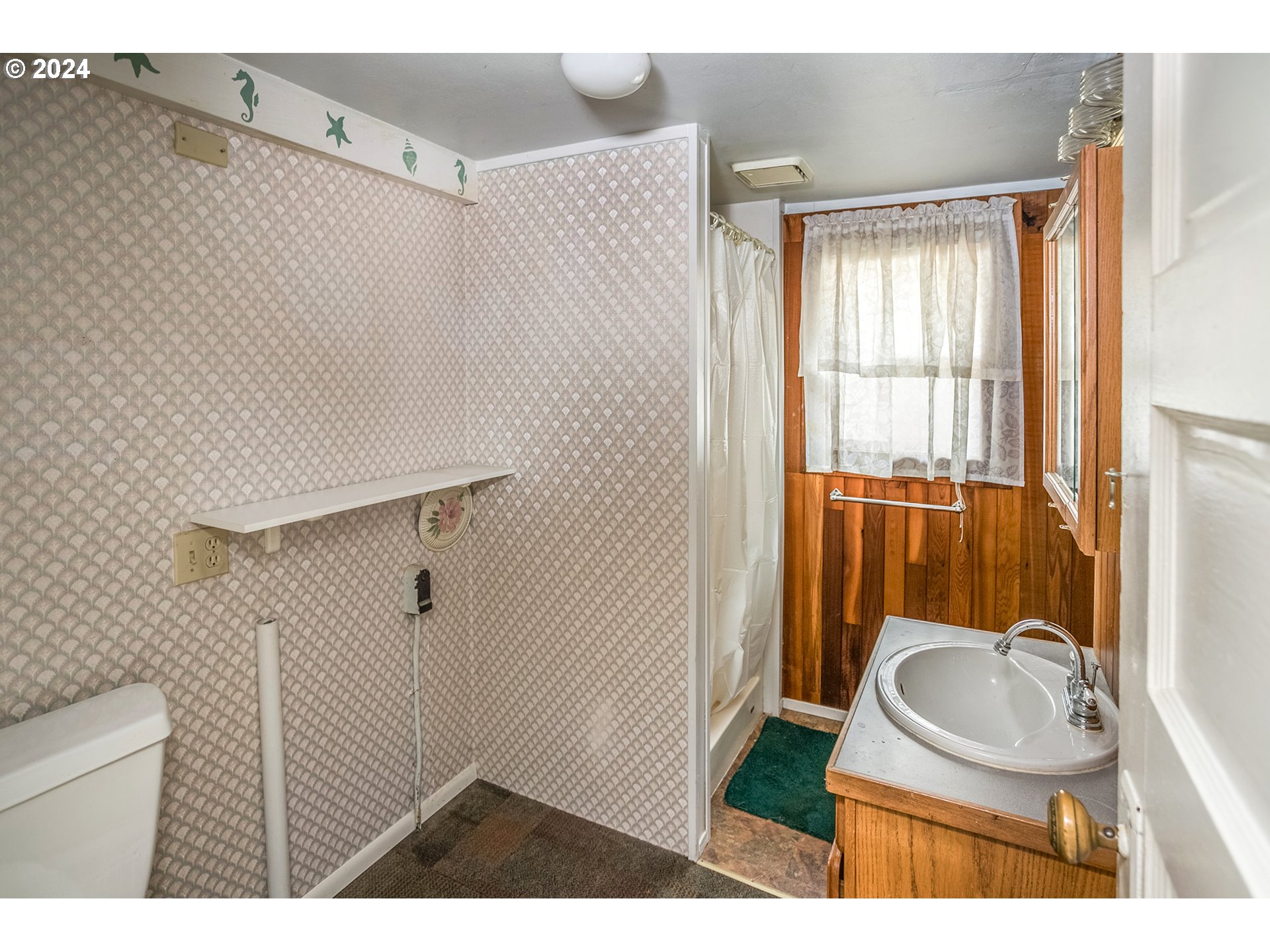 Bathroom with patterned wallpaper, a curtained shower, and a sink vanity against wood-paneled walls.