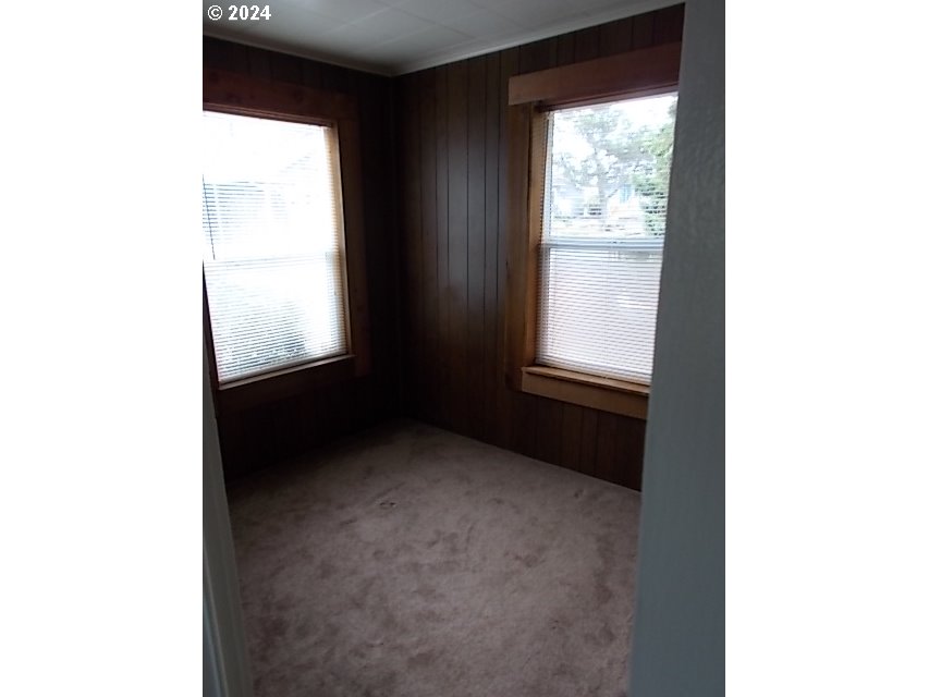 Empty carpeted room with dark wood-paneled walls and two windows with blinds.