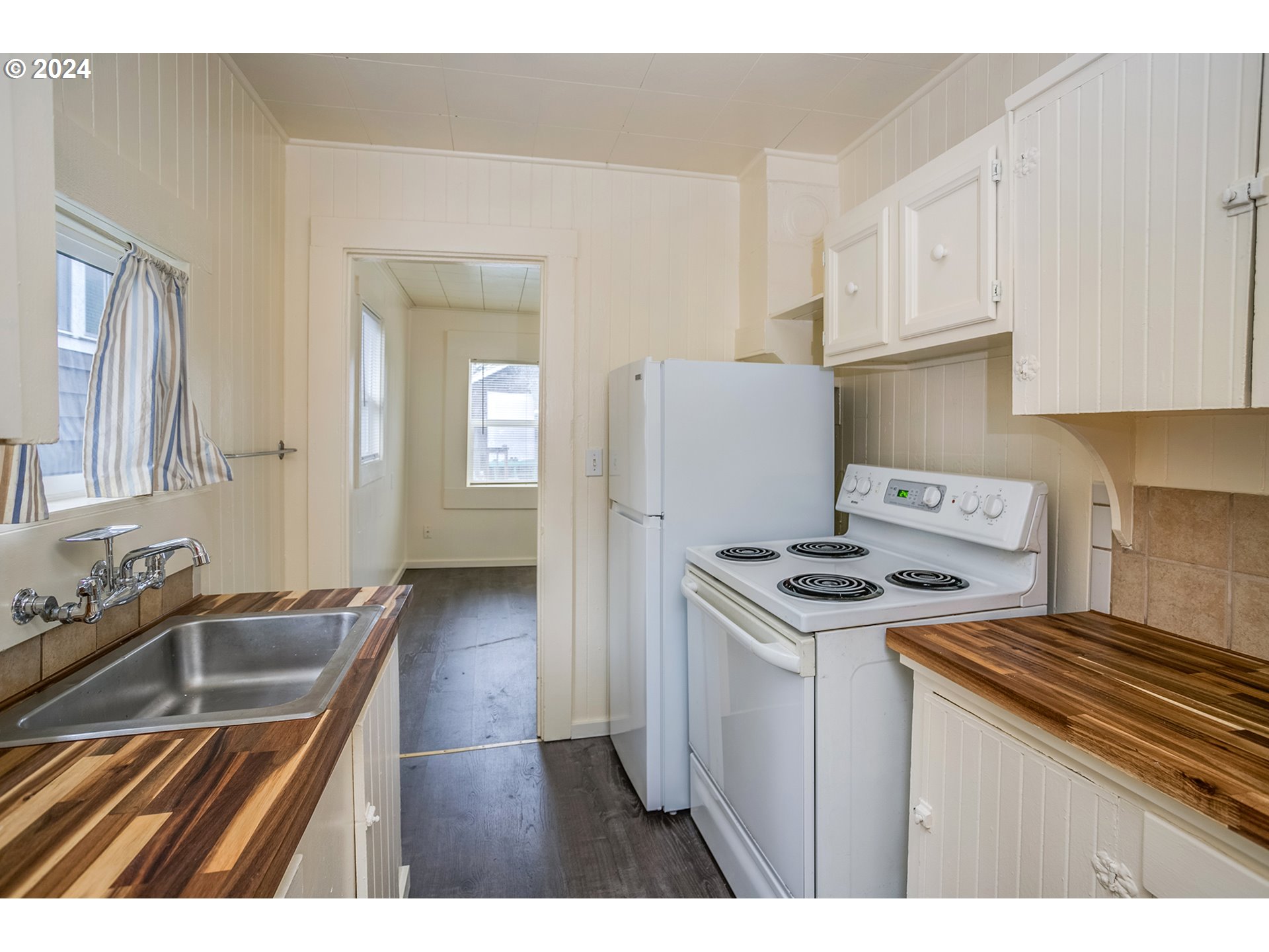 Kitchen with butcher-block counters, a stainless-steel sink, white refrigerator, and electric range.