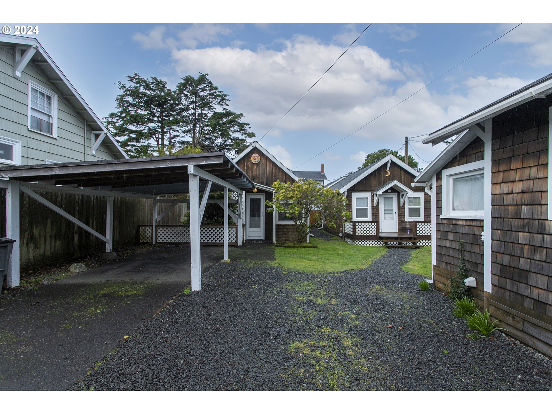 Small shingle-sided cottages surround a gravel courtyard with a covered carport.