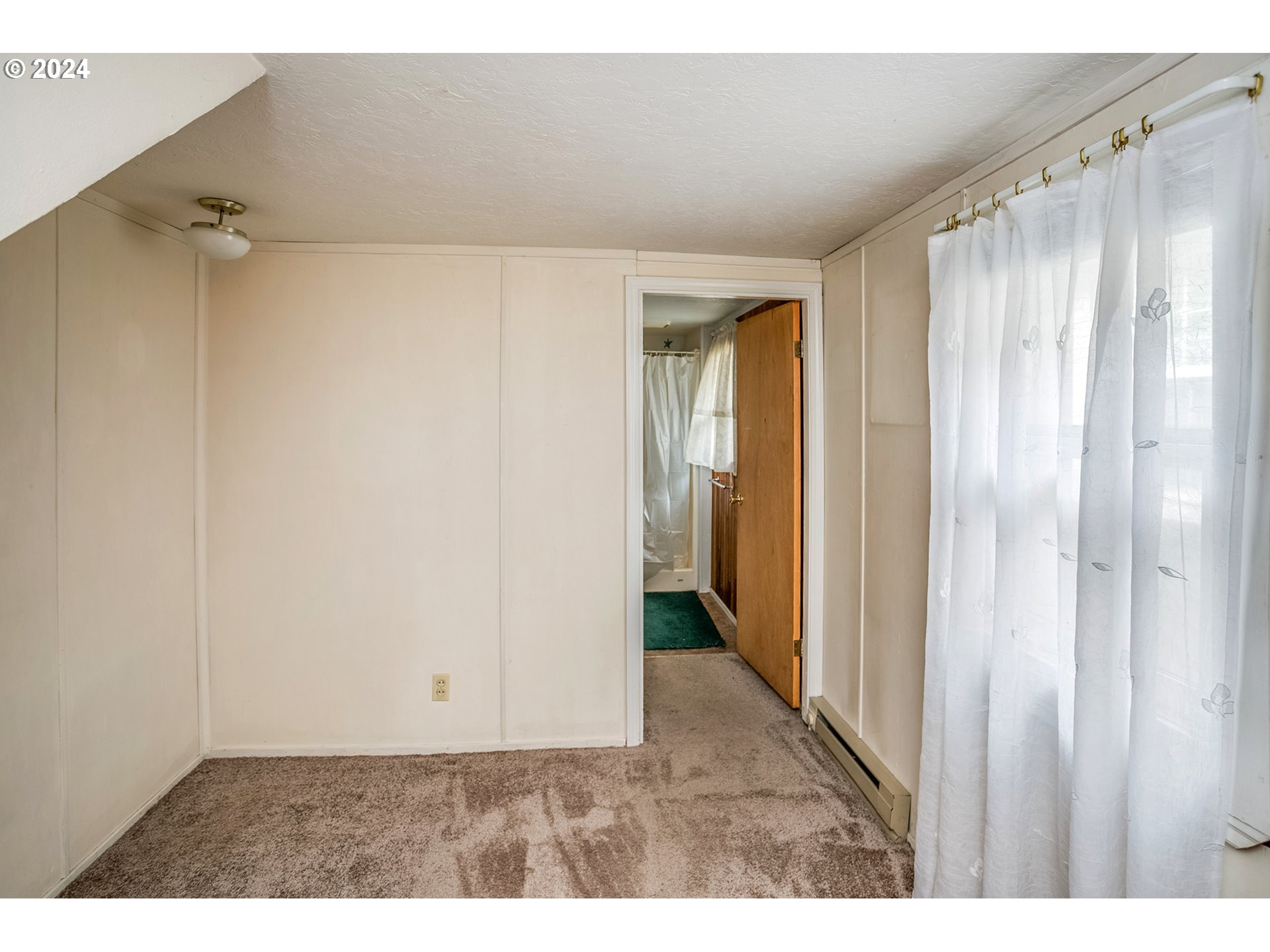 Empty carpeted room with sheer curtains and an open doorway to a bathroom.