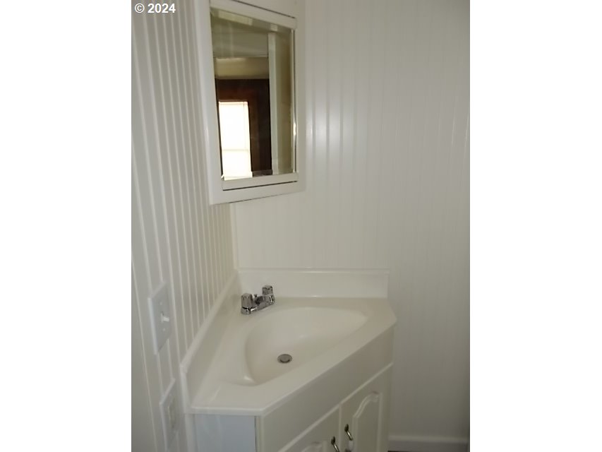 White corner bathroom vanity with integrated sink, chrome faucet, and framed mirror.