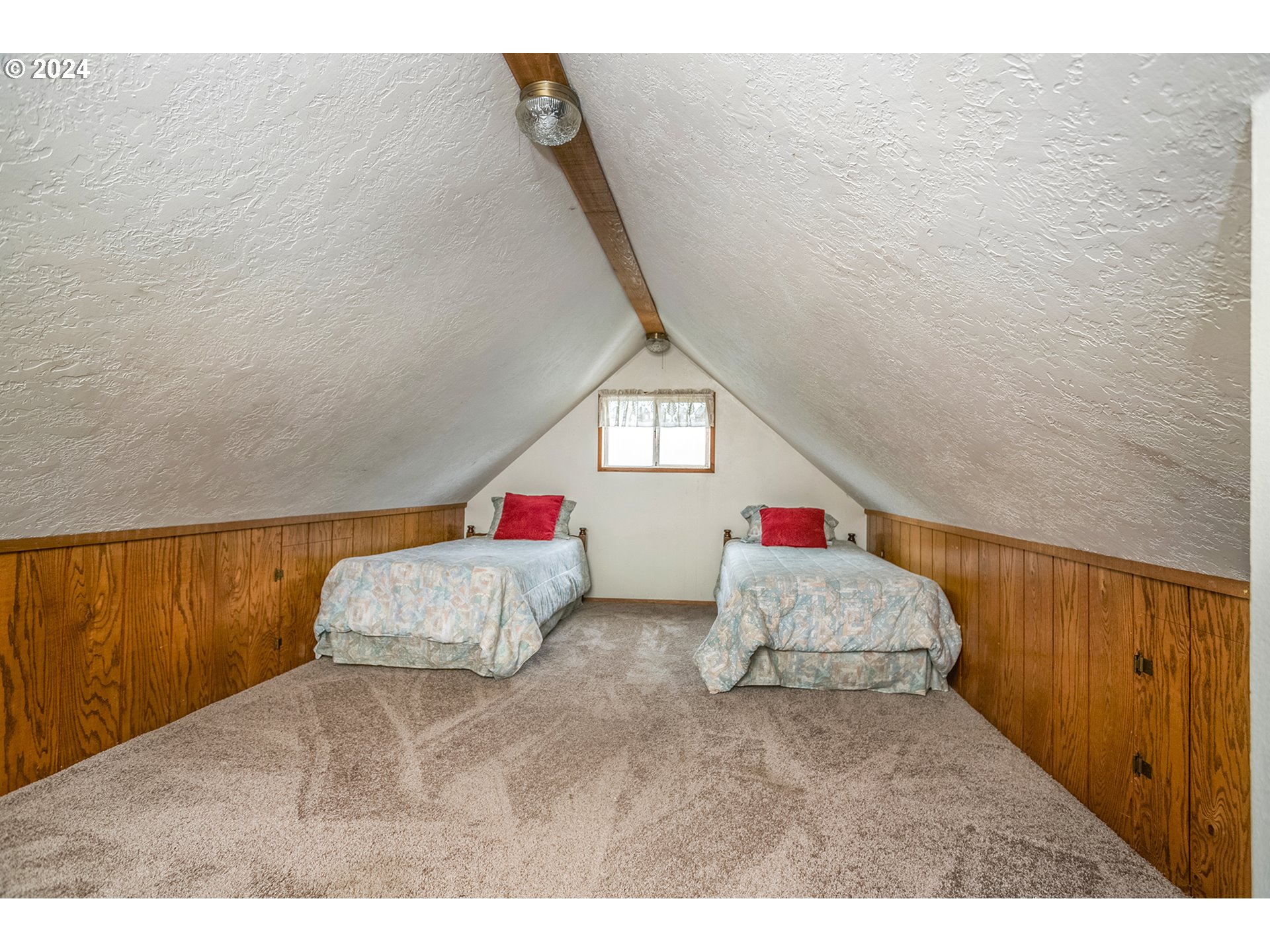 Attic bedroom with two twin beds, red pillows, and wood-paneled walls.